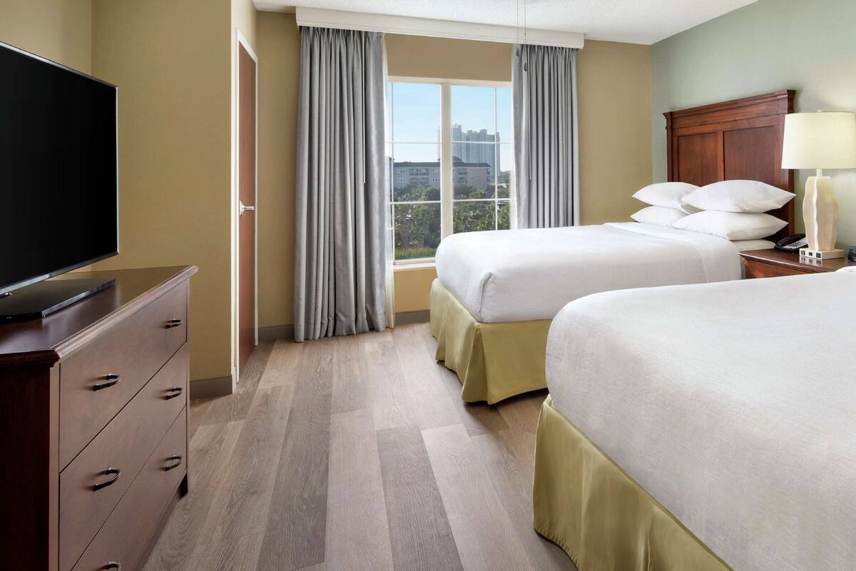 Une chambre d’hôtel avec deux lits, une télévision, une commode et une fenêtre avec des rideaux.