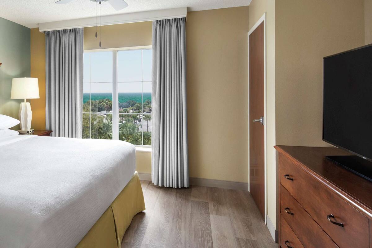 Une chambre d’hôtel avec un grand lit, une télévision, une fenêtre avec des rideaux et une vue sur la ville.