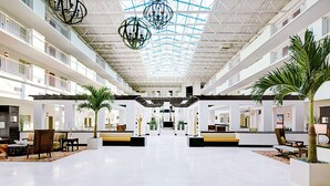 Eine geräumige Lobby mit hoher Decke, mehreren Sitzbereichen und einer zentralen Treppe.