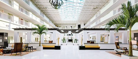 Un hall d’entrée spacieux avec un plafond haut, de nombreux espaces de détente et un escalier central.