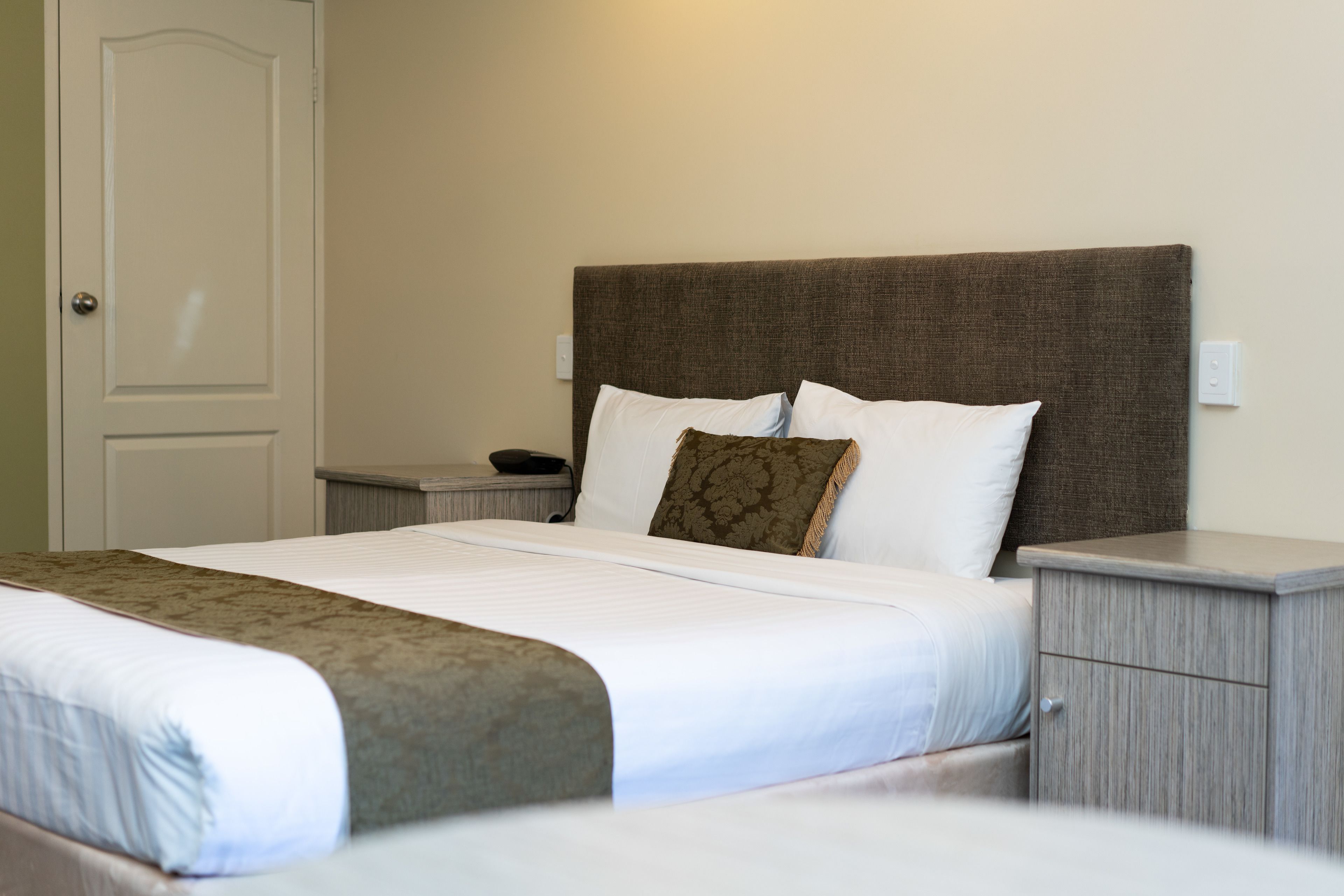 A neatly made bed with a brown headboard, white bedding, and a brown decorative pillow.
