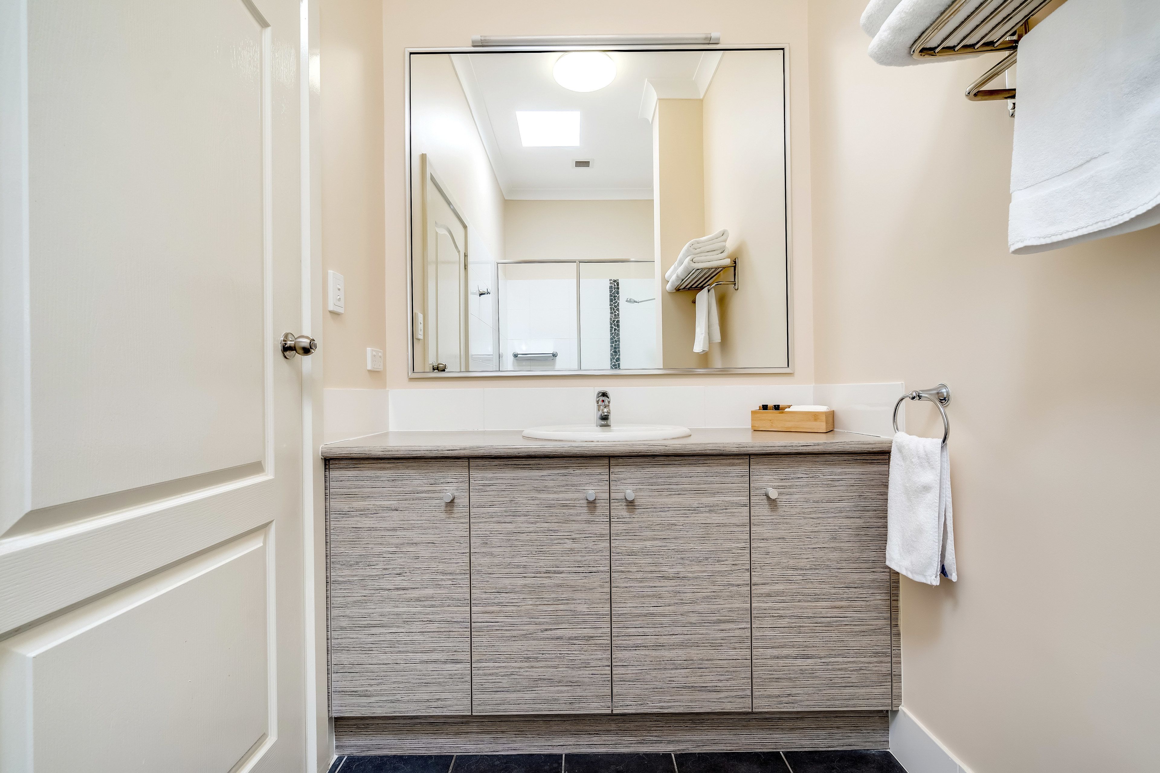 A bathroom with a large mirror, a sink, and a towel rack.