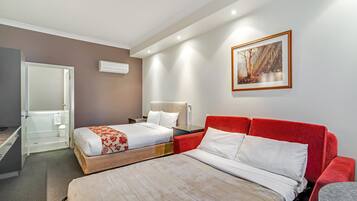 Una habitación de hotel con dos camas, un sofá rojo, una mesita pequeña y un cuadro en la pared.
