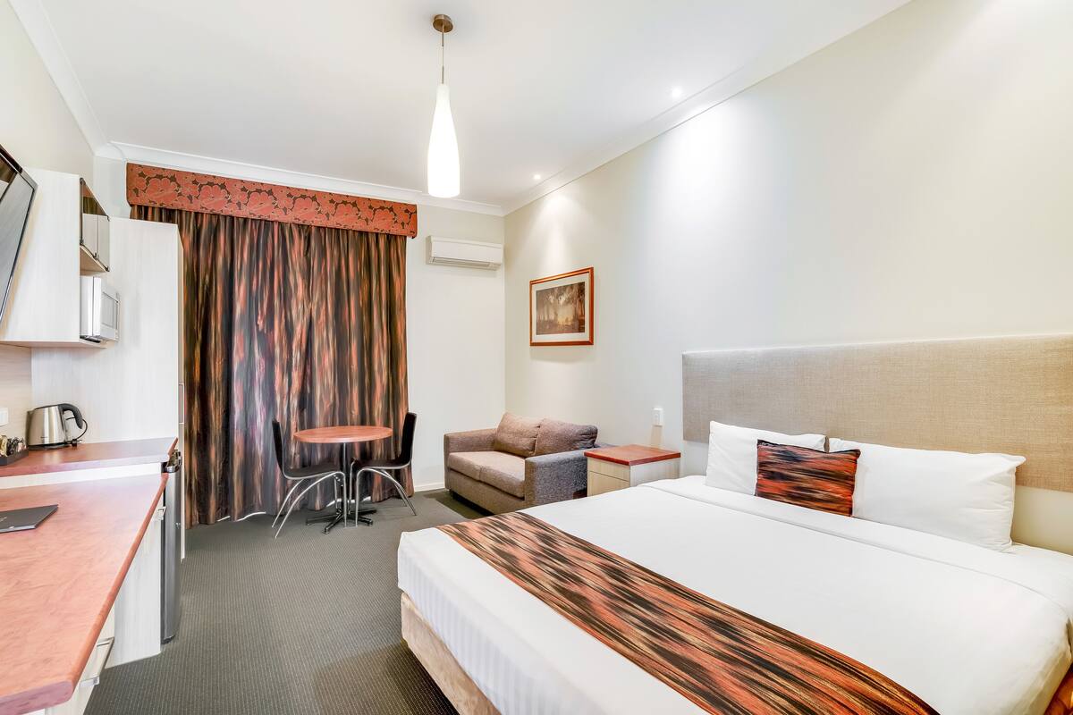 A hotel room with a bed, a desk, a chair, a small table, and a couch.