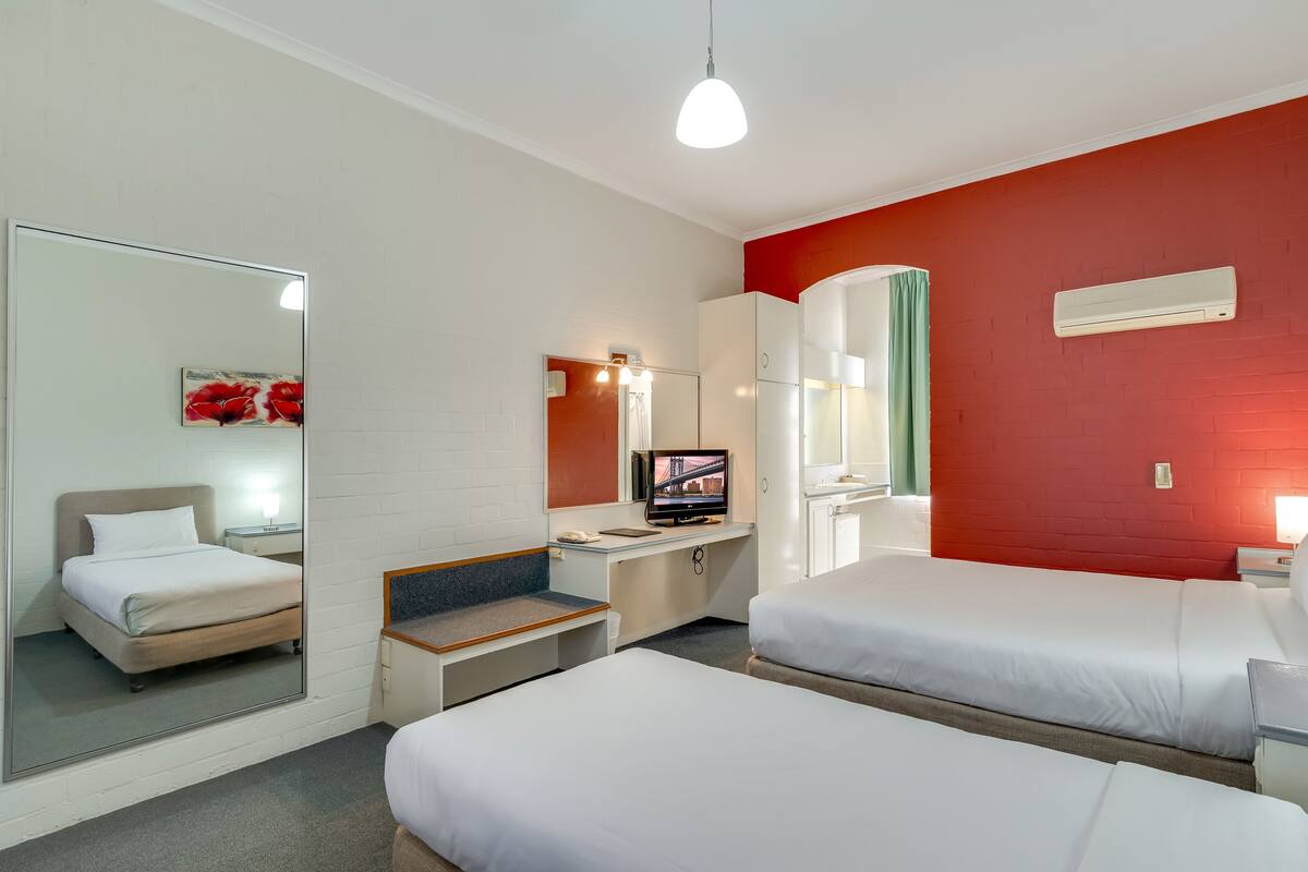 A hotel room with two beds, a desk, a mirror, and a television.