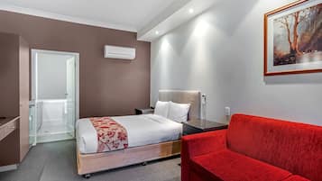 Habitació d'hotel amb un llit, un sofà vermell, un quadre a la paret i una porta que condueix a un bany.