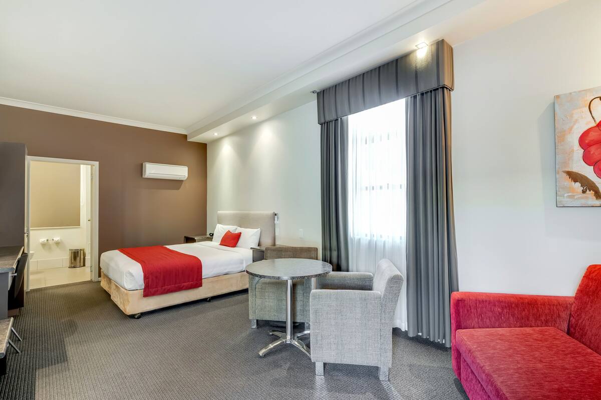 A hotel room with a bed, a small round table, a sofa, a chair, and a painting on the wall.