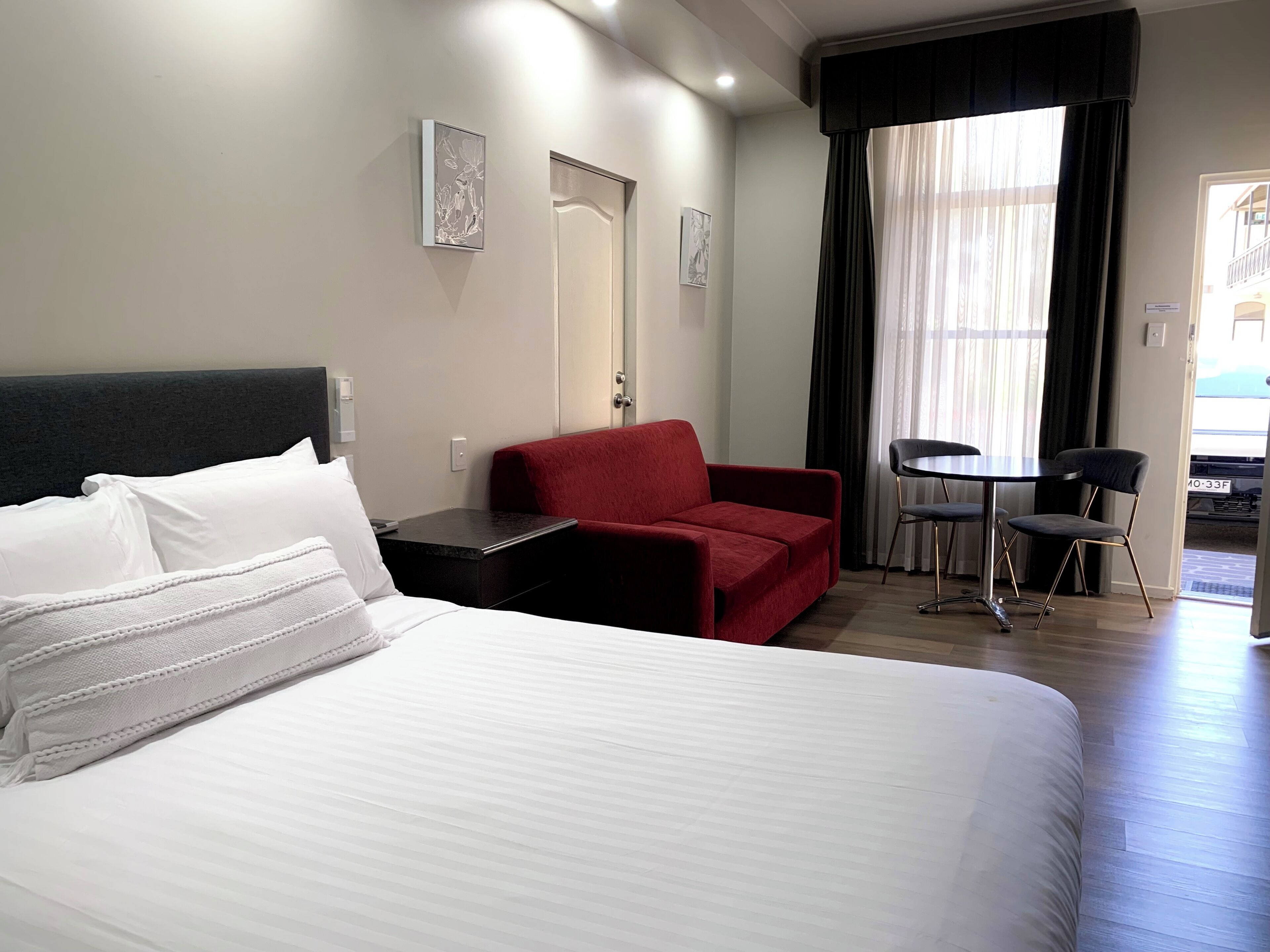 A hotel room with a bed, a red sofa, a small table, and a chair.