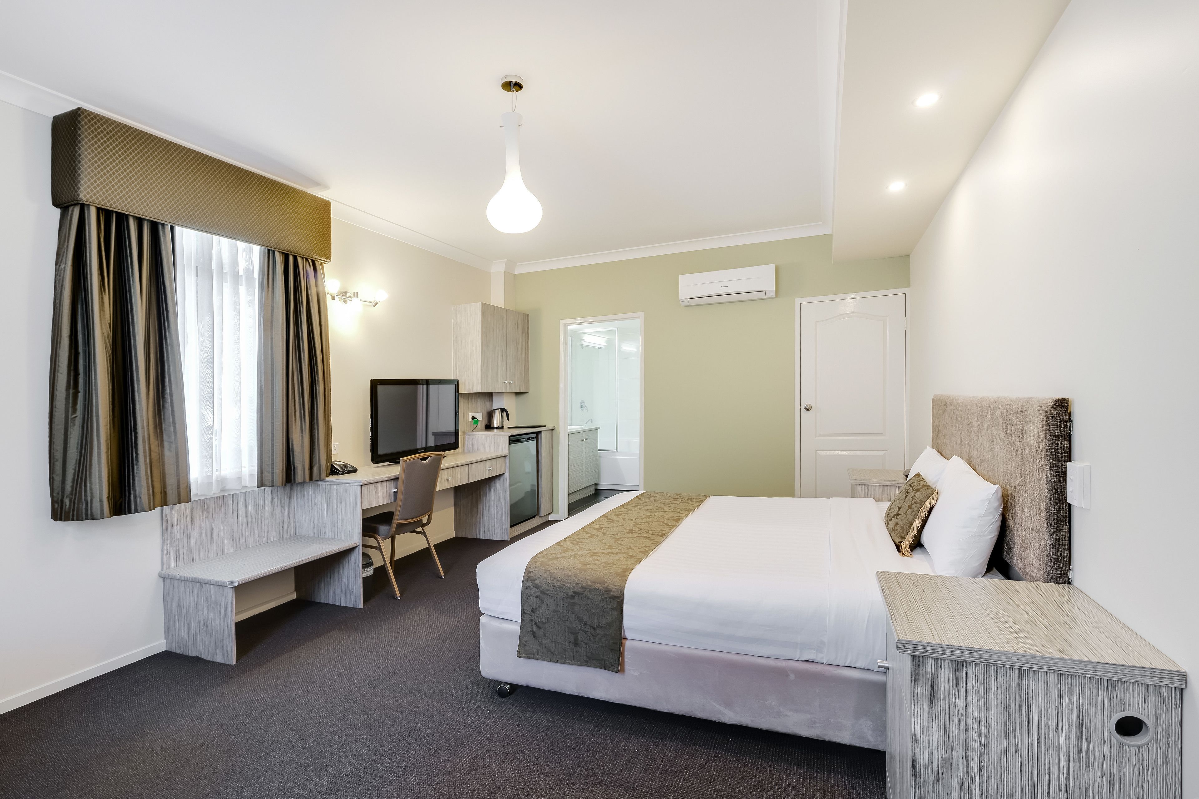 Habitación de hotel con cama, escritorio, silla y televisor.