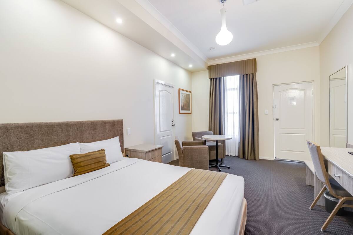 A hotel room with a large bed, a desk, a chair, and a small table.
