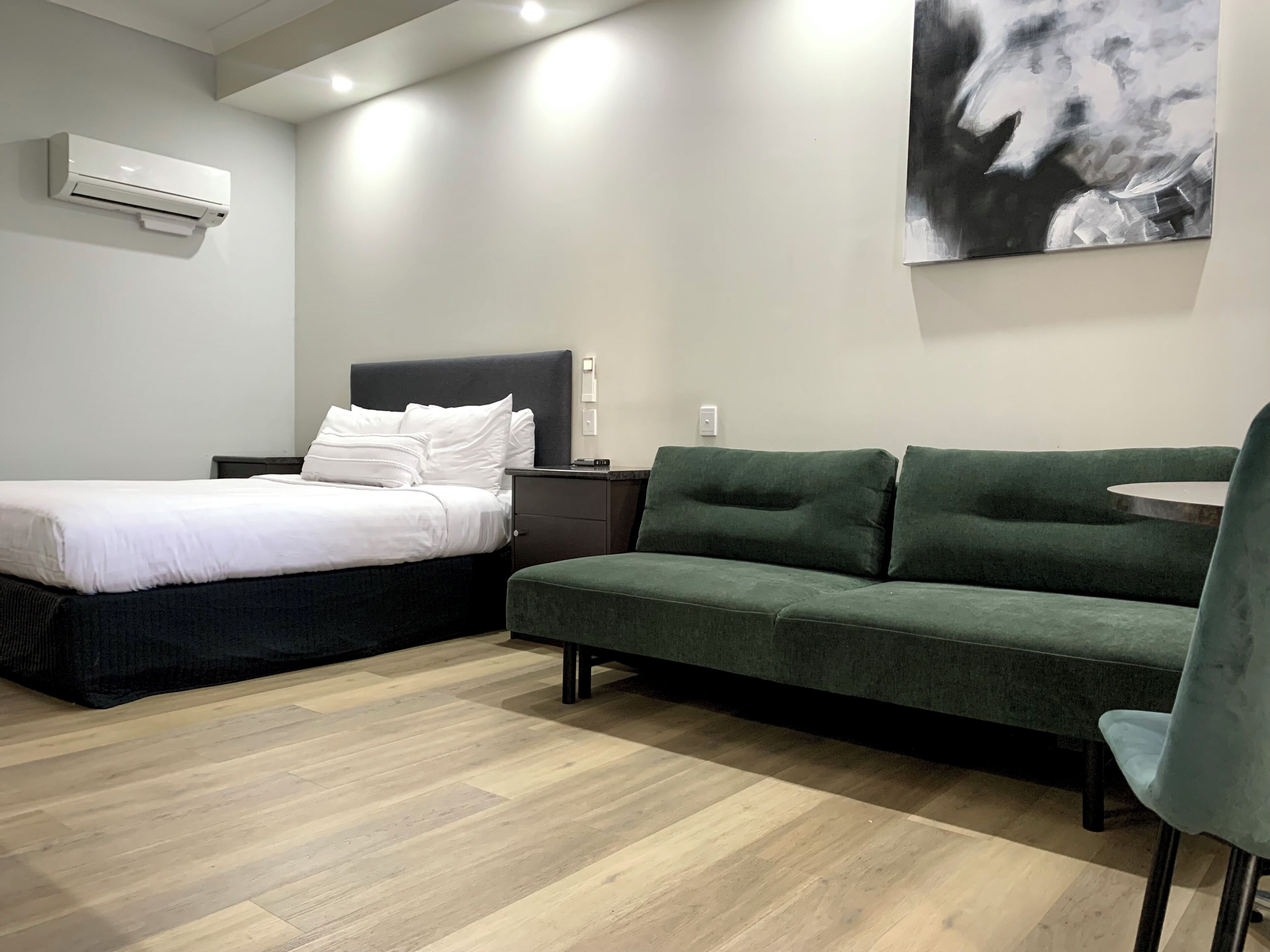 Un dormitorio con una cama, un sofá verde, una mesita y un aire acondicionado instalado en la pared.