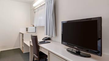 A hotel room with a desk, chair, television, and a window with curtains.