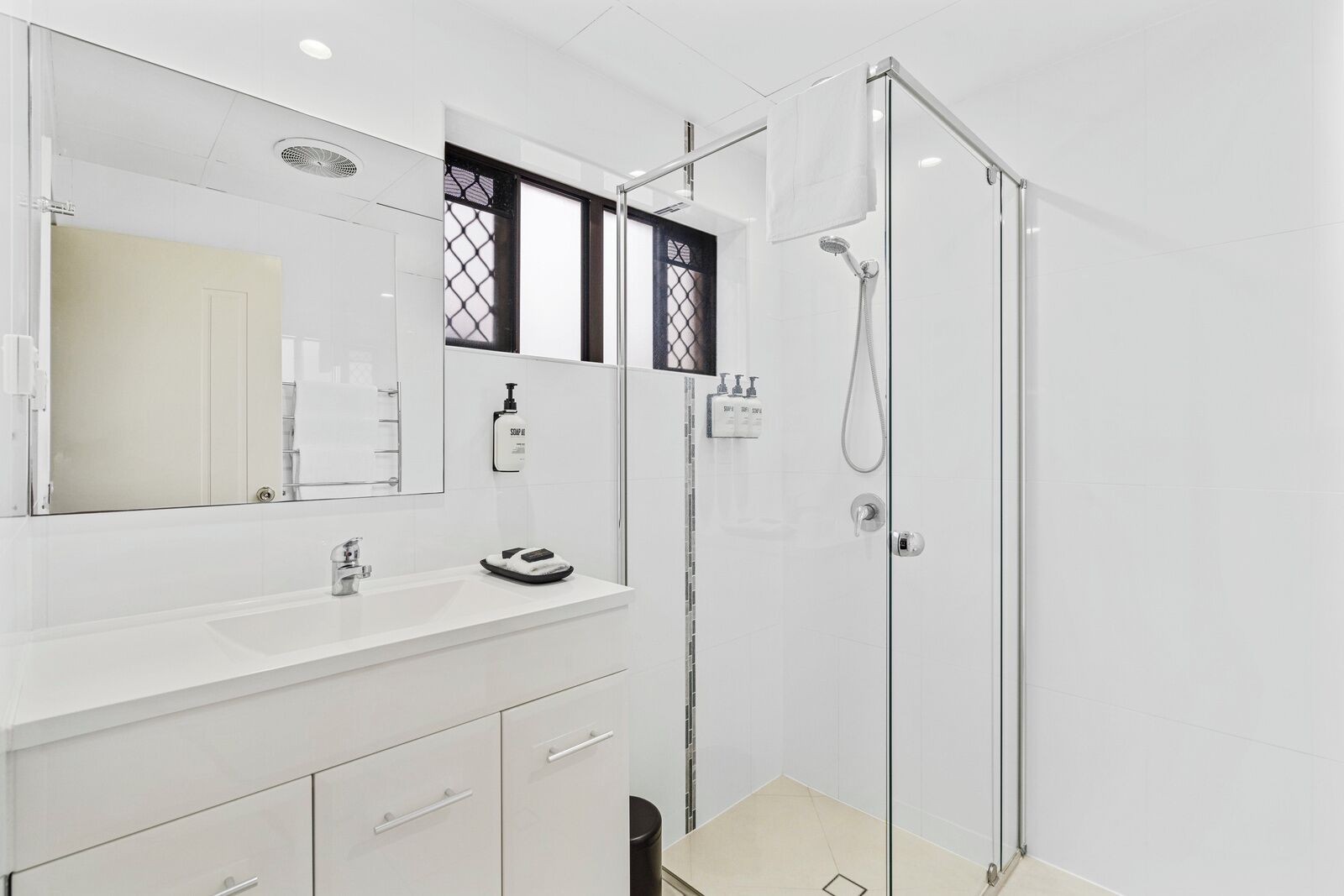 Uma casa de banho moderna com chuveiro em cabine de vidro, um espelho grande e um lavatório branco com gavetas de arrumação.