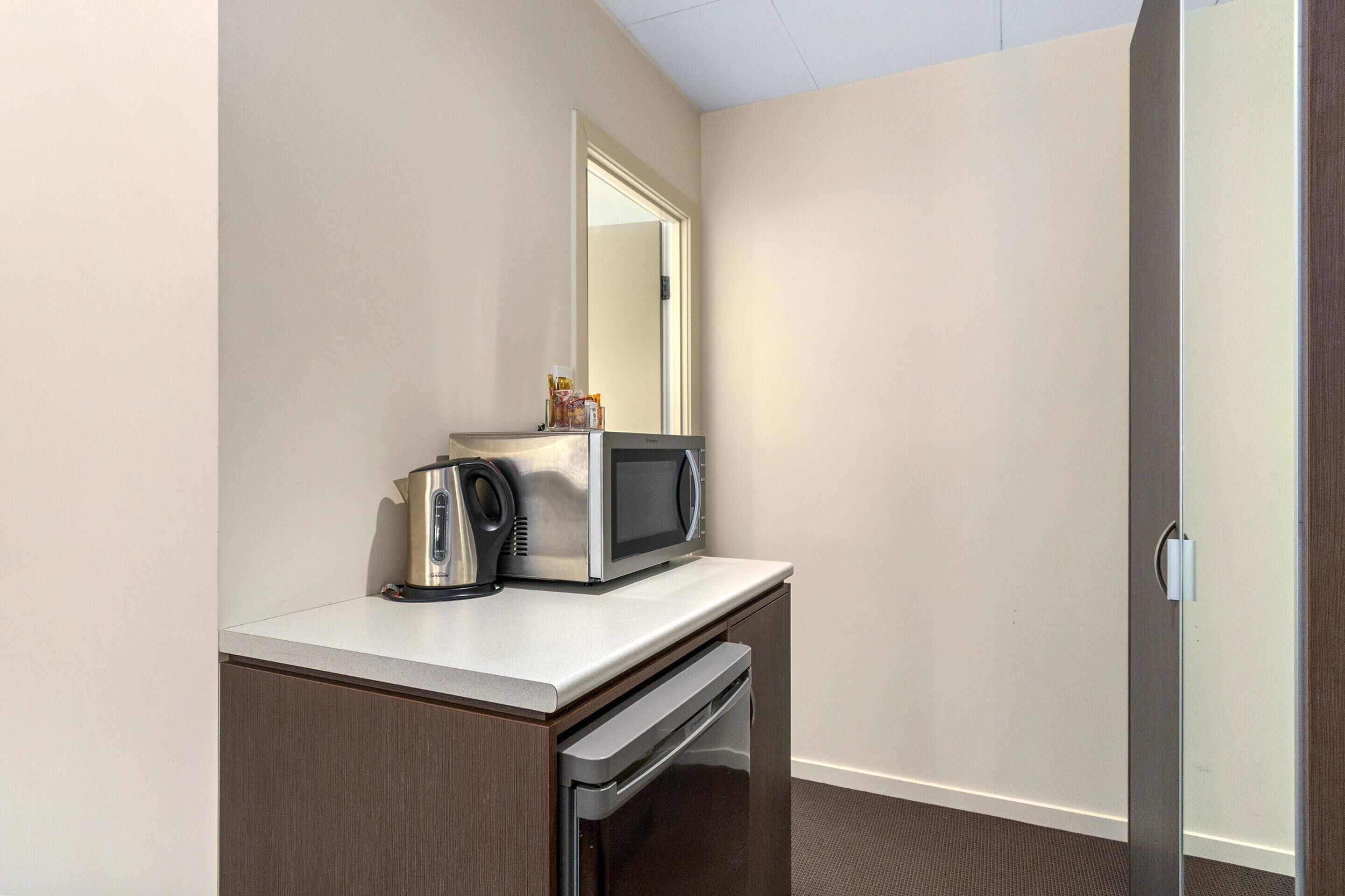 A kitchenette with a microwave, kettle, and coffee maker on a countertop.