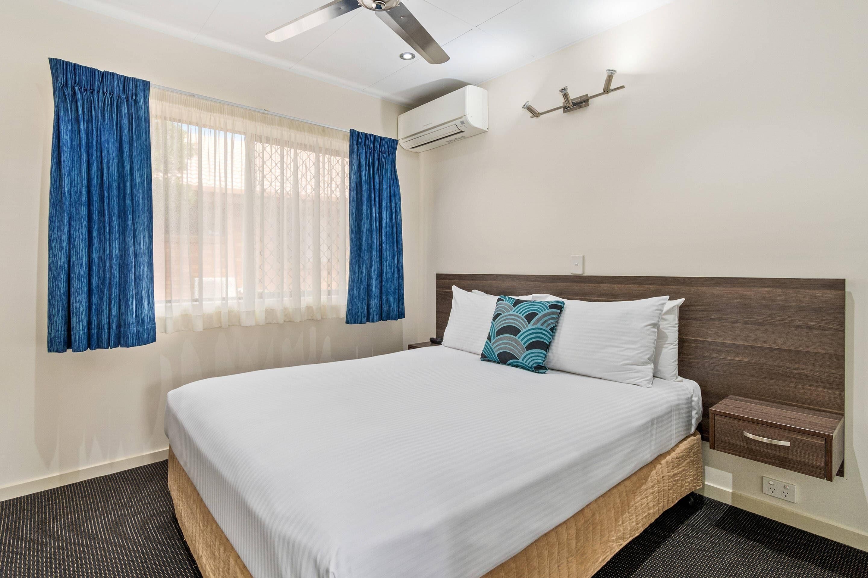 Una habitación de hotel con cama, mesita de noche, aire acondicionado montado en la pared y ventilador de techo.