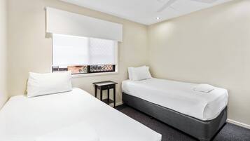 A hotel room with two beds, a ceiling fan, a window with blinds, and a small table.