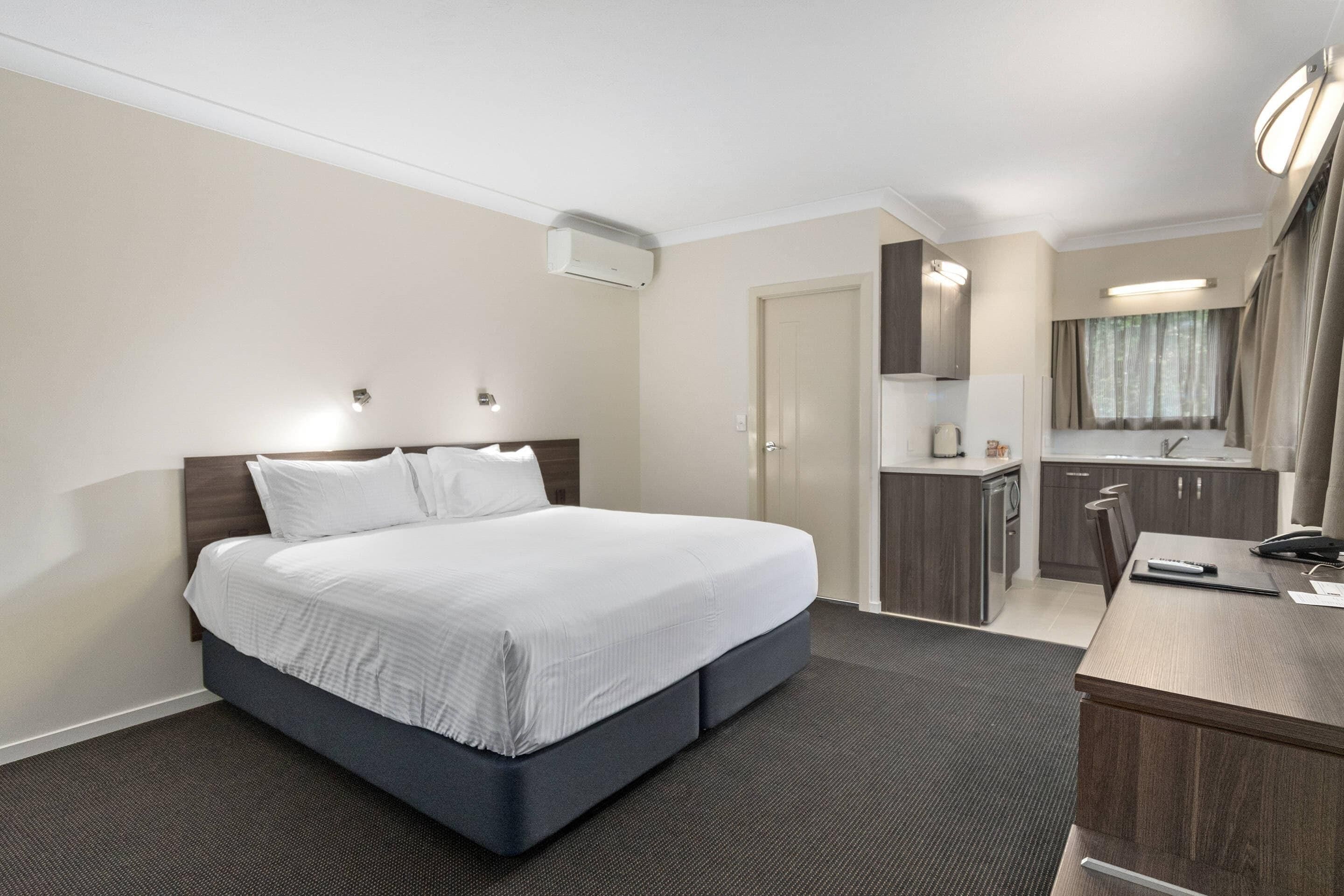 A hotel room with a bed, a desk, a kitchenette, and a bathroom.