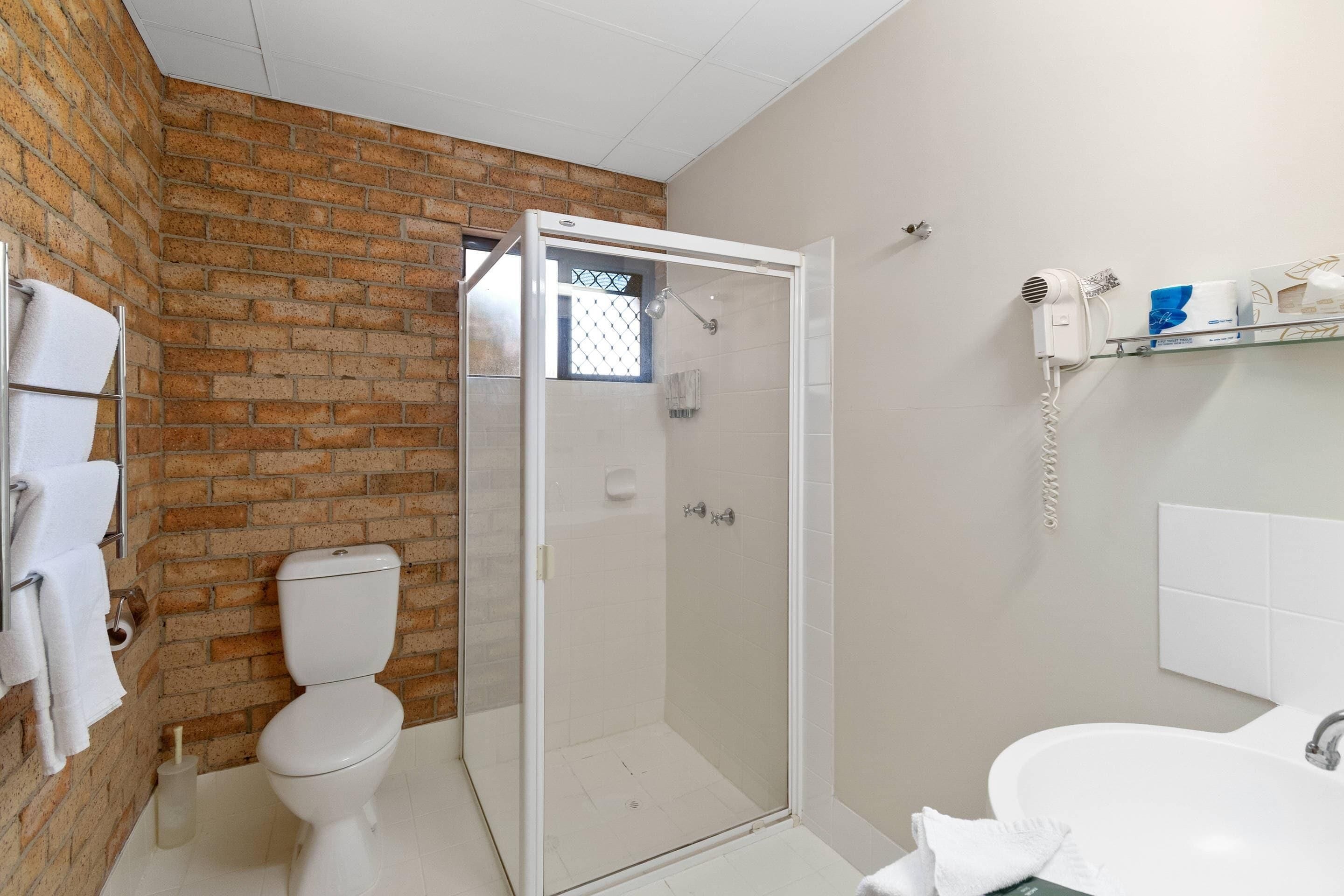 Ein Badezimmer mit Toilette, Duschkabine, Waschbecken und einem Fön auf einem Regal.