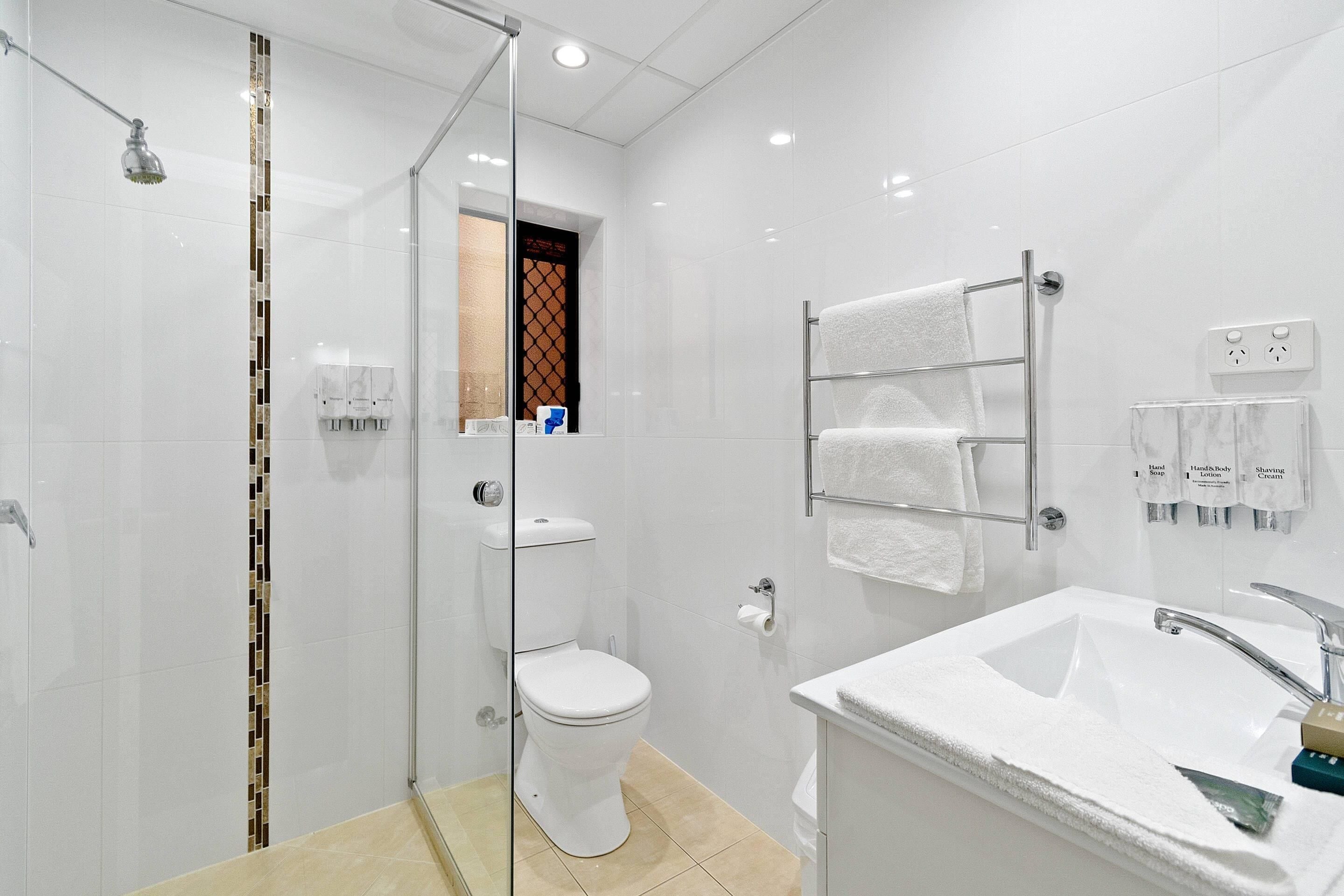 Un baño moderno con ducha envuelta en vidrio, un lavamanos blanco con encimera de mármol y un perchero con varias toallas.