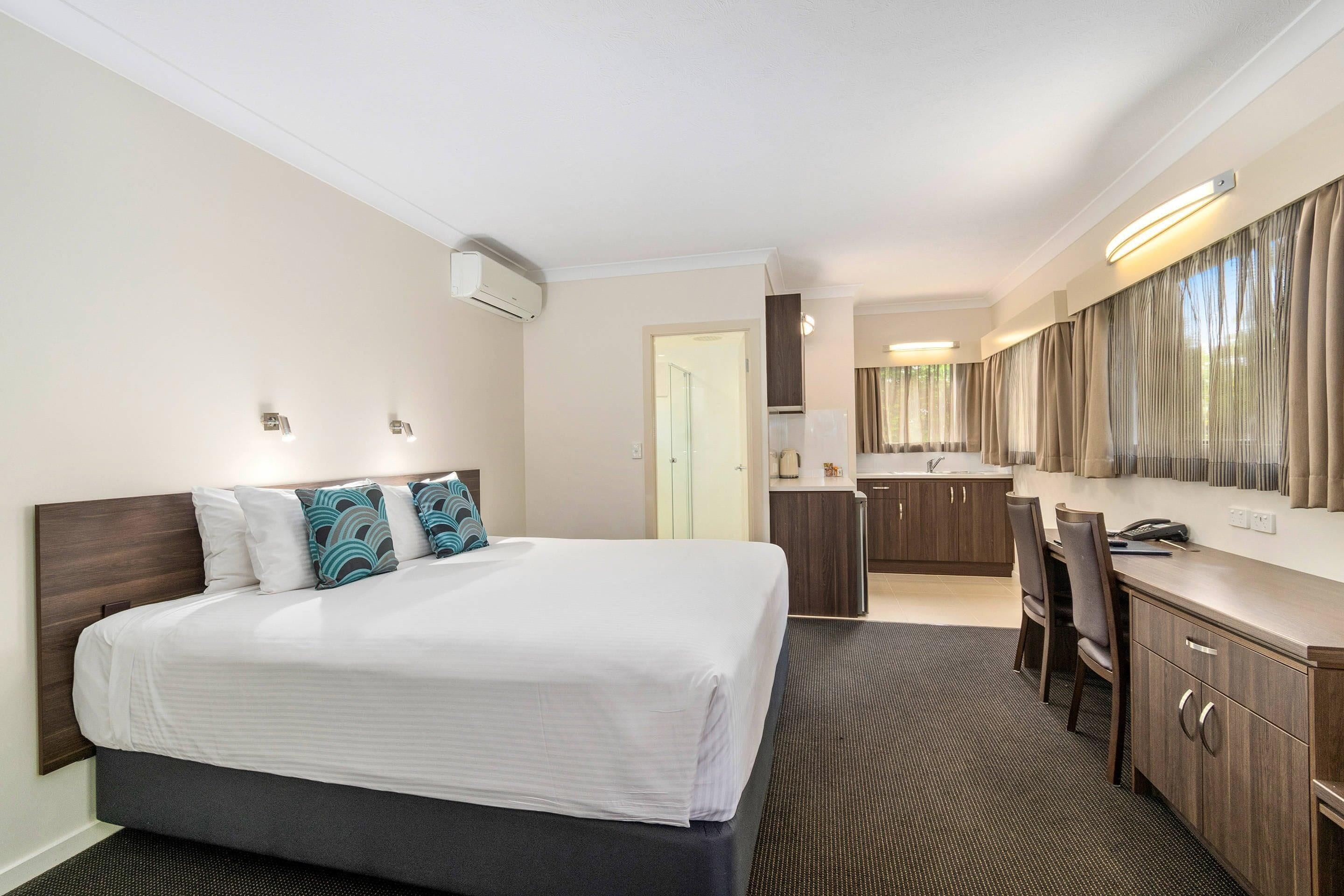 A hotel room with a bed, a desk, a chair, a kitchenette, and a bathroom.