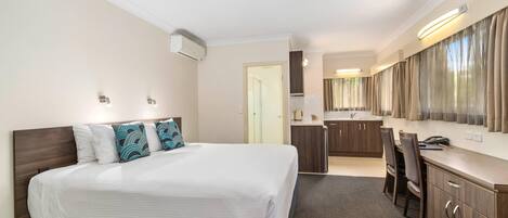 A hotel room with a bed, a desk, a chair, a kitchenette, and a bathroom.