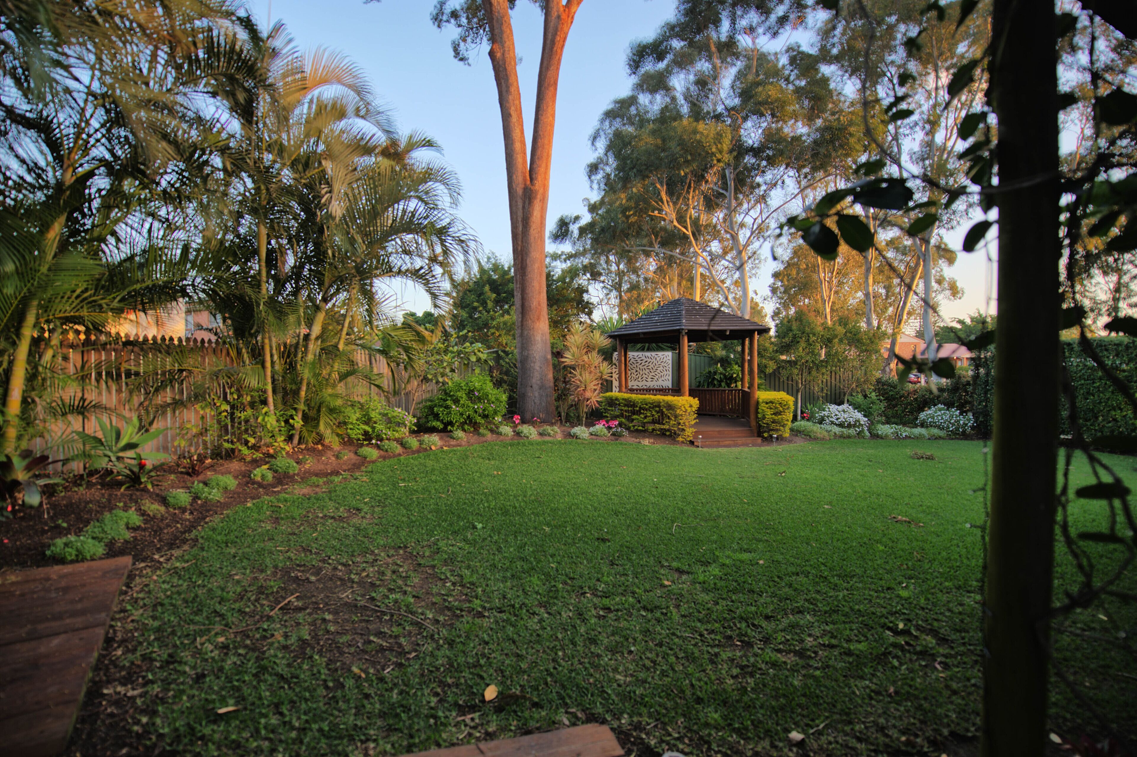 A well-maintained garden with a gazebo, various trees, and a clear sky.