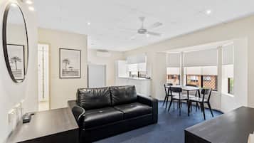 Une chambre d’hôtel moderne, dotée d’un canapé en cuir noir, d’une table à manger avec des chaises, d’un coin cuisine et de grandes fenêtres donnant sur l’extérieur.