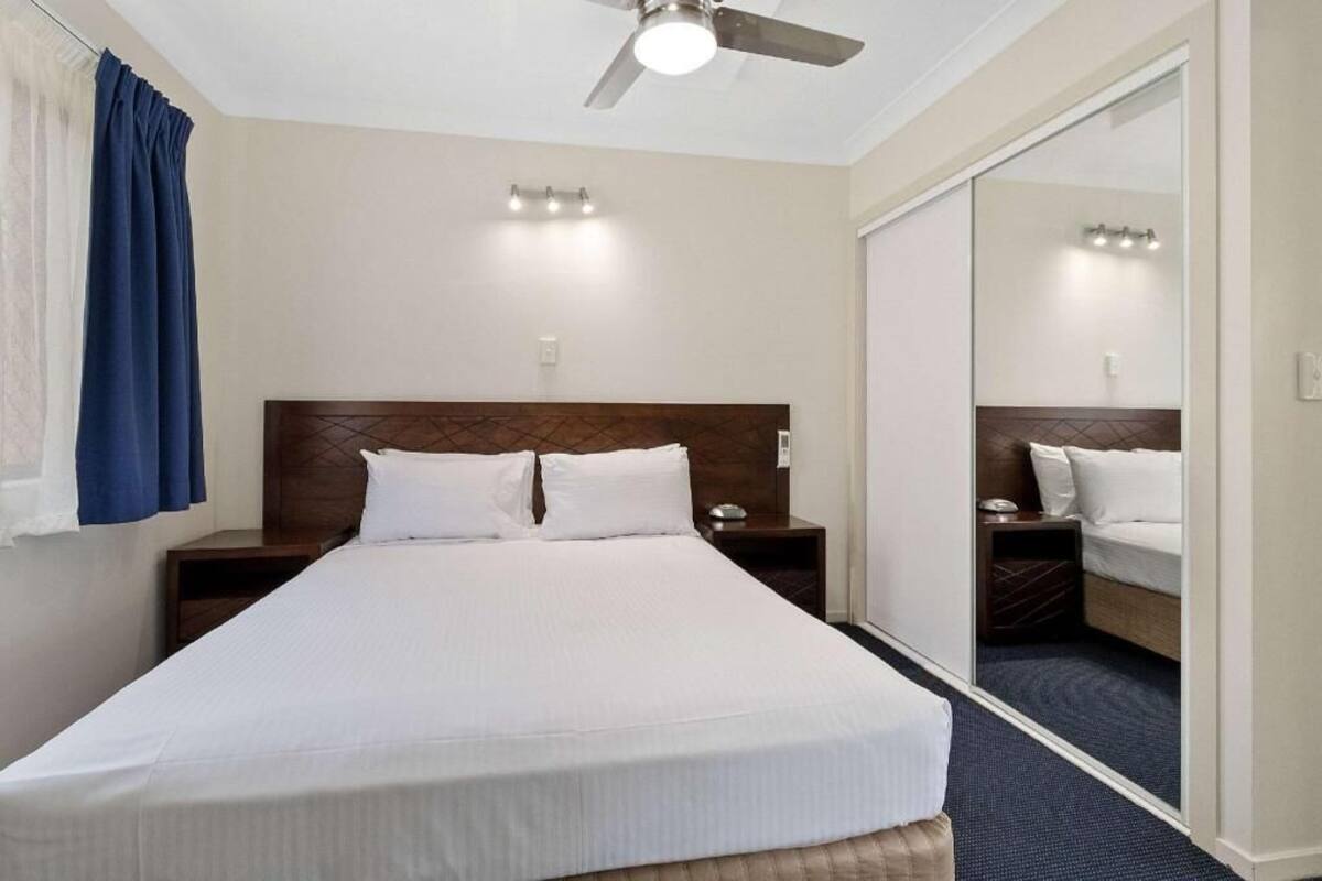 A hotel room with a large bed, a ceiling fan, bedside lamps, a mirror, and a sliding door.