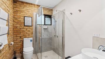 Ein modernes Badezimmer mit Backsteinwand, Duschkabine, Toilette und Waschbecken.