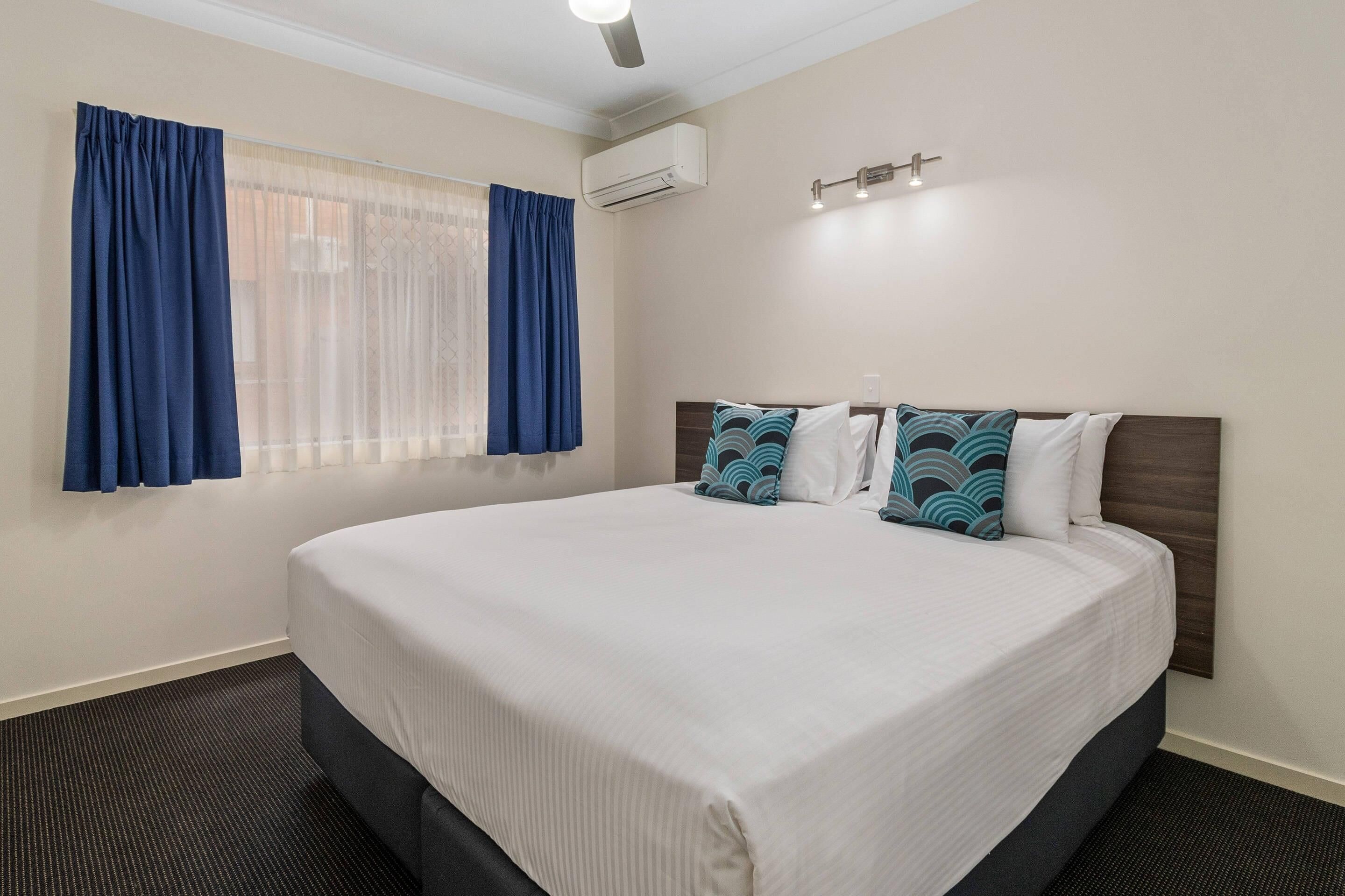 Habitación de hotel con cama grande, ventana con cortinas, equipo de aire acondicionado y lámpara fijada a la pared.