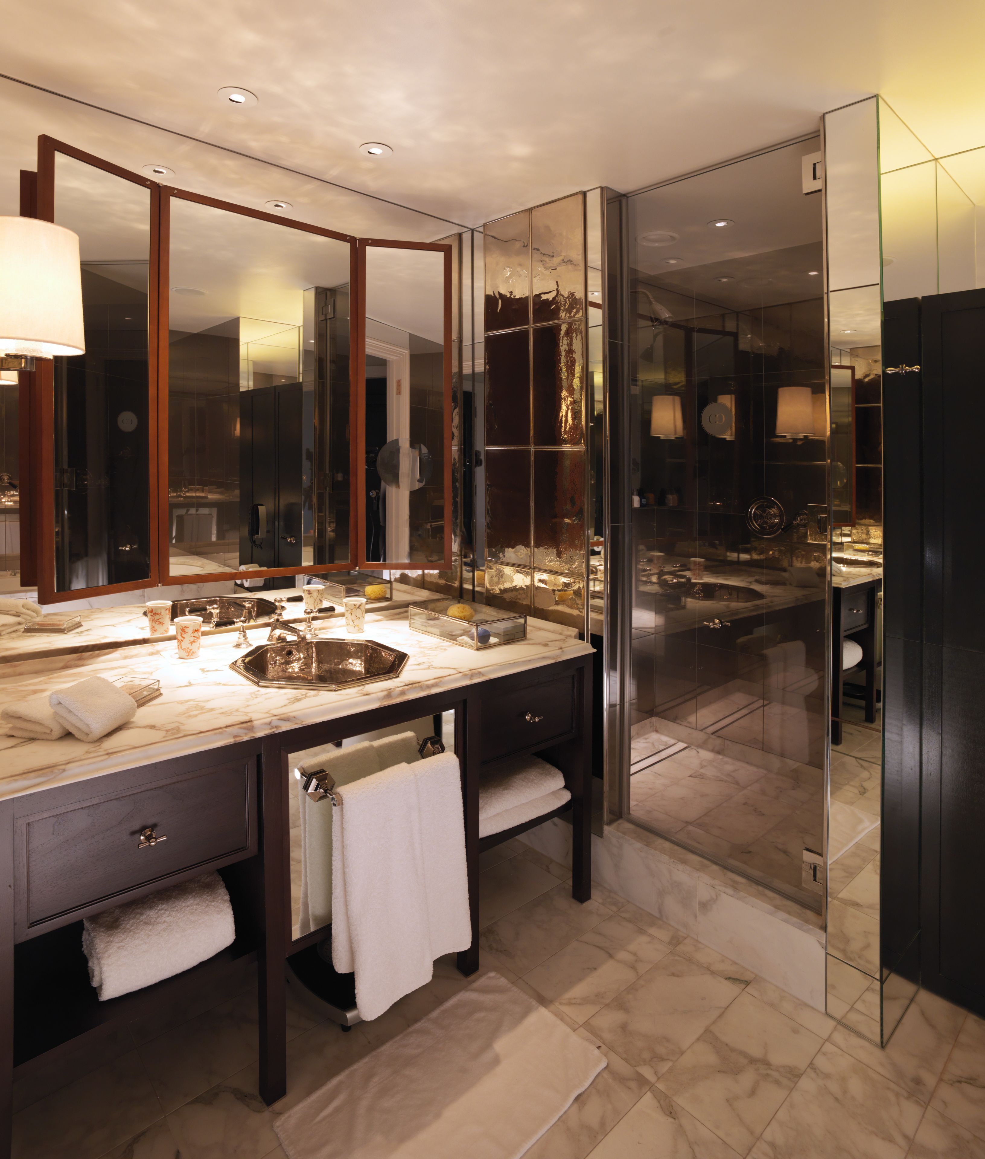 A modern bathroom with a large mirror, a marble sink, and a glass-enclosed shower area.
