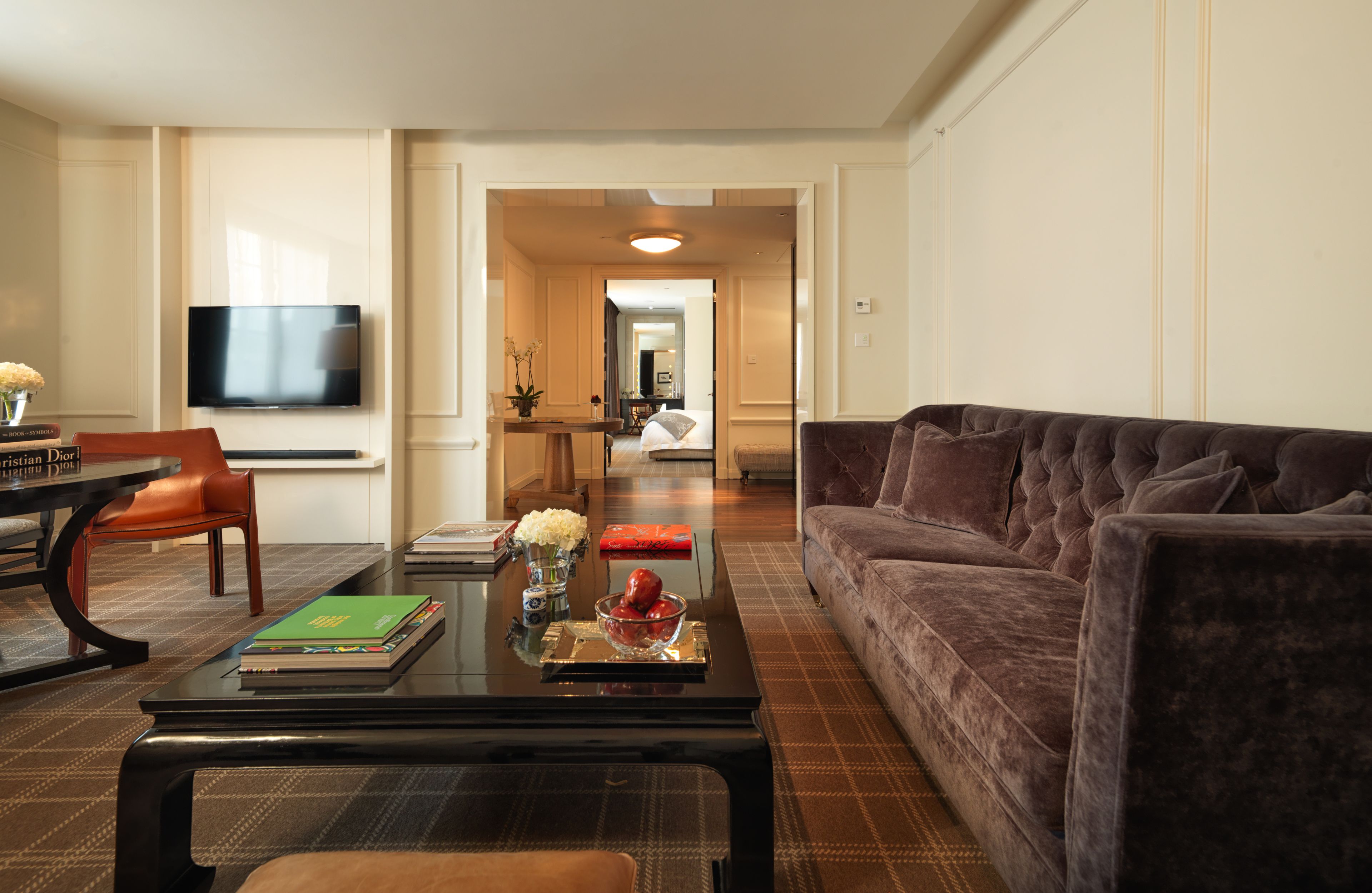 Een moderne woonkamer met een donkerbruine bank, een glazen salontafel en een flatscreen televisie aan de wand.
