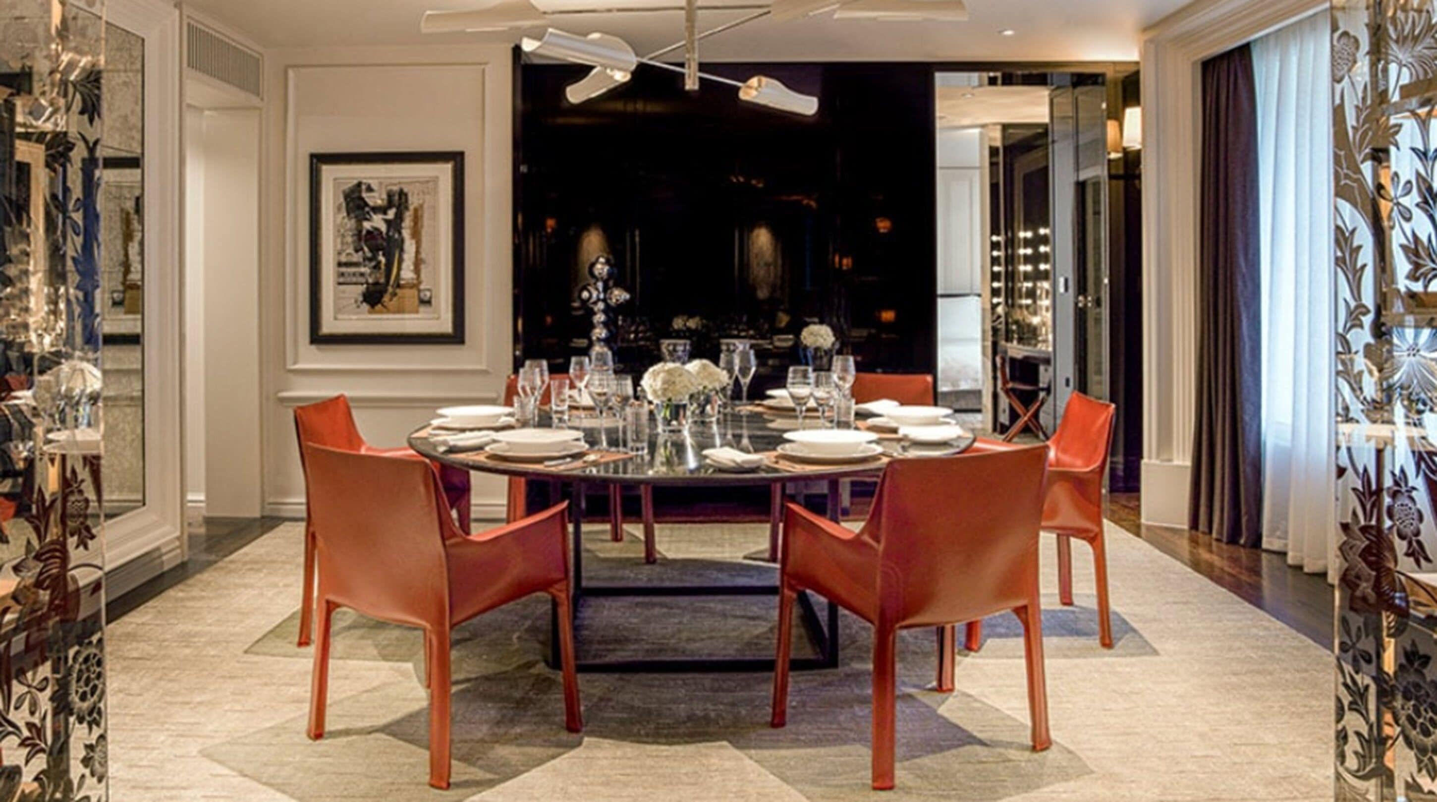A dining area with a round table set for four, surrounded by orange chairs.