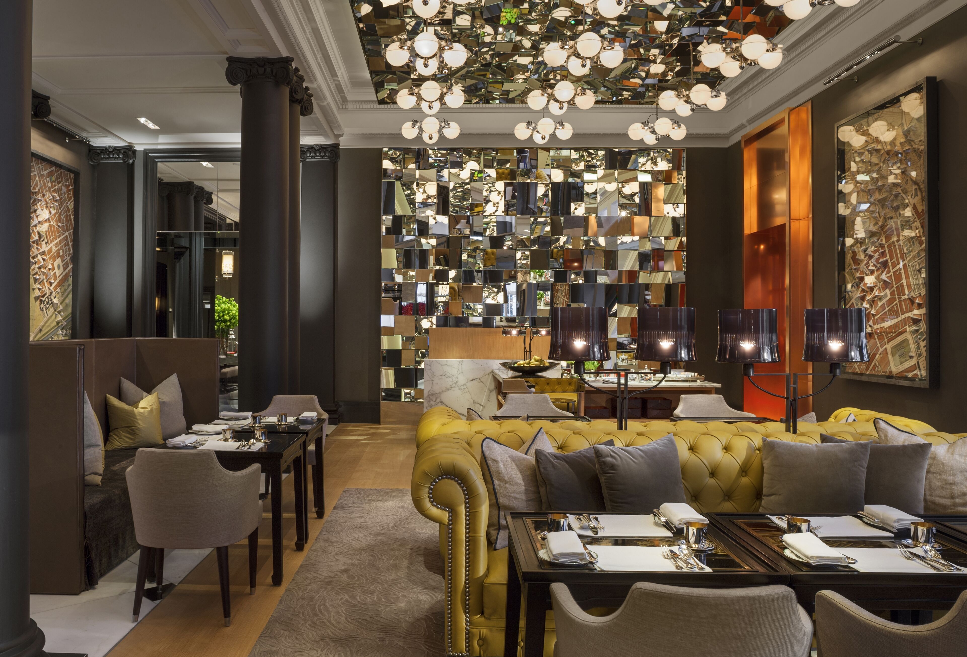 A modern hotel lobby with a central seating area, a bar, and a large mirror wall.