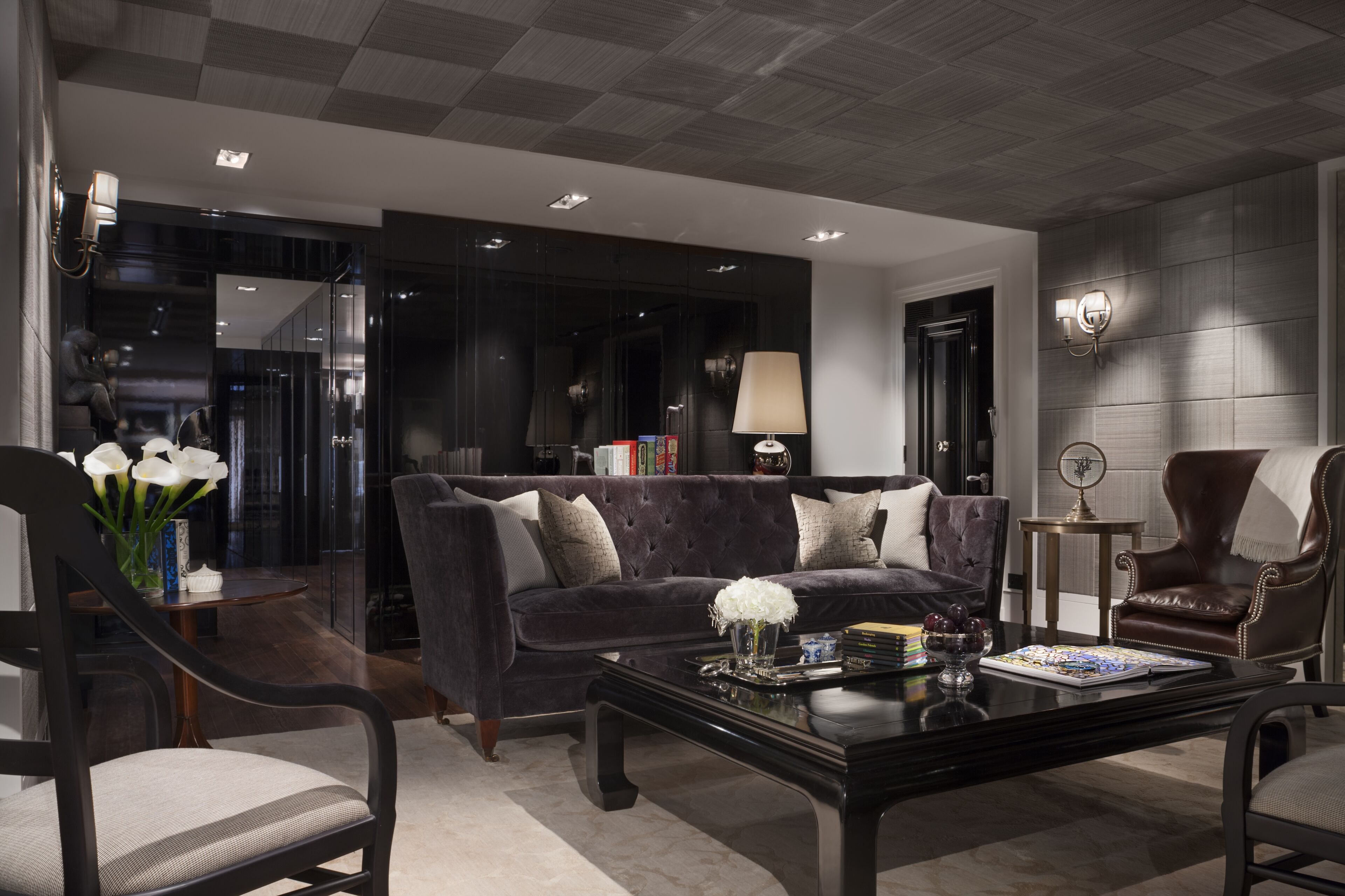 Una sala de estar moderna con un sofá de color oscuro, dos sillones, una mesita de centro y una estantería.