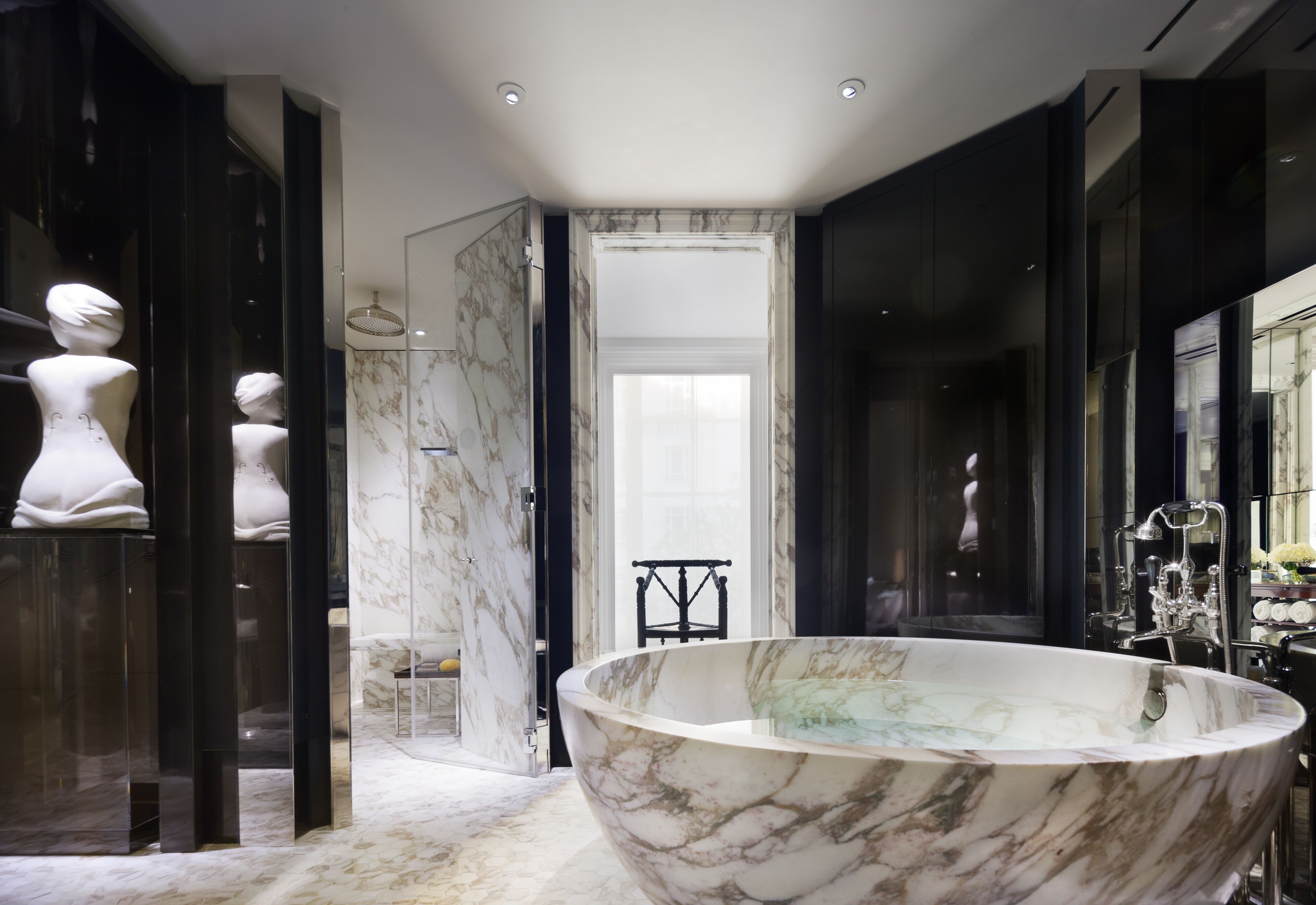 A modern bathroom with a large freestanding bathtub, marble walls, and a glass shower enclosure.