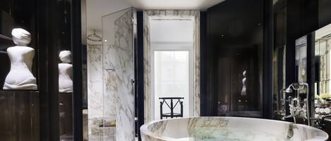 A modern bathroom with a large freestanding bathtub, marble walls, and a glass shower enclosure.