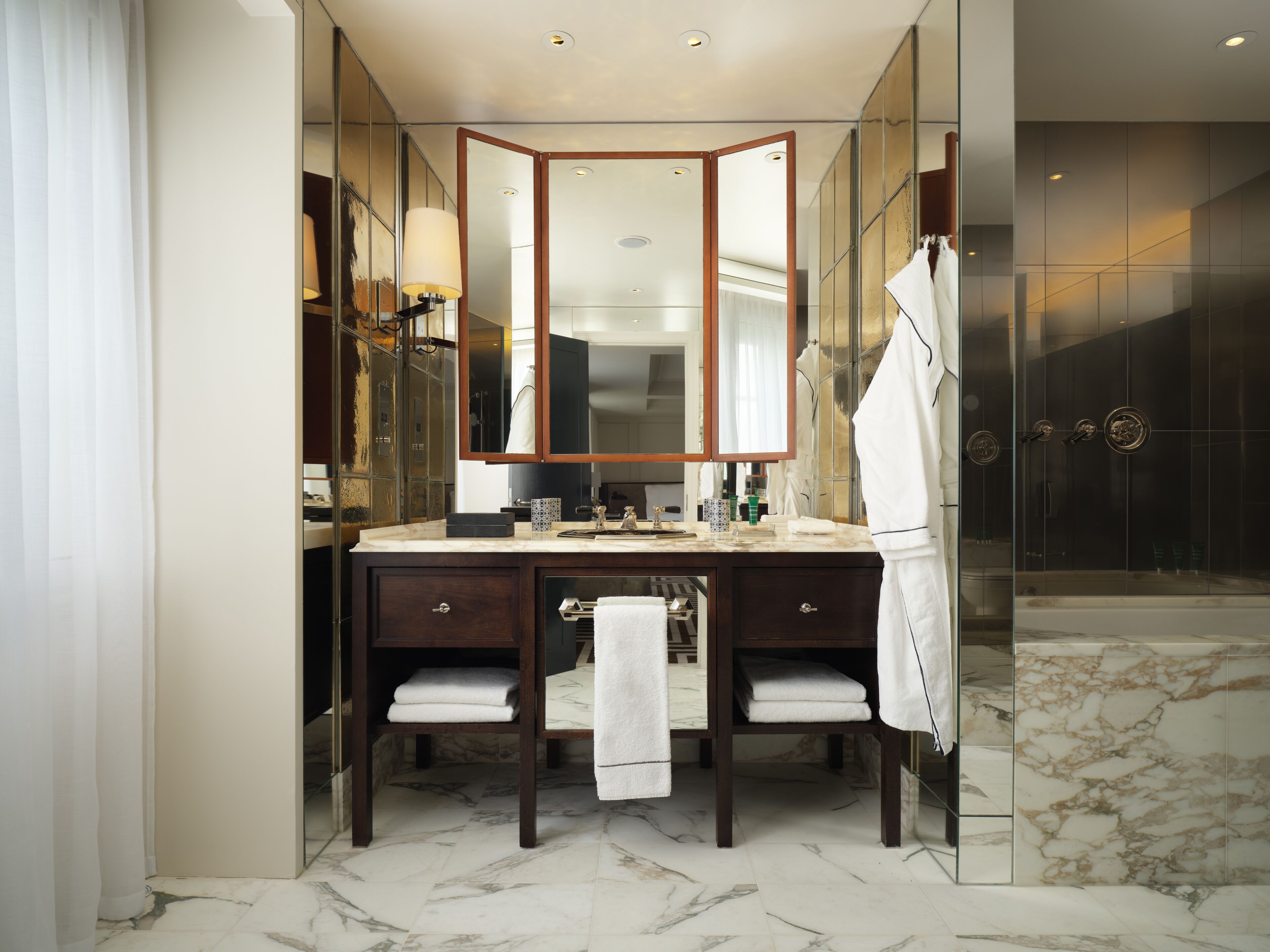 A modern bathroom with a marble floor, a large mirror, a vanity with two sinks, and a glass shower enclosure.