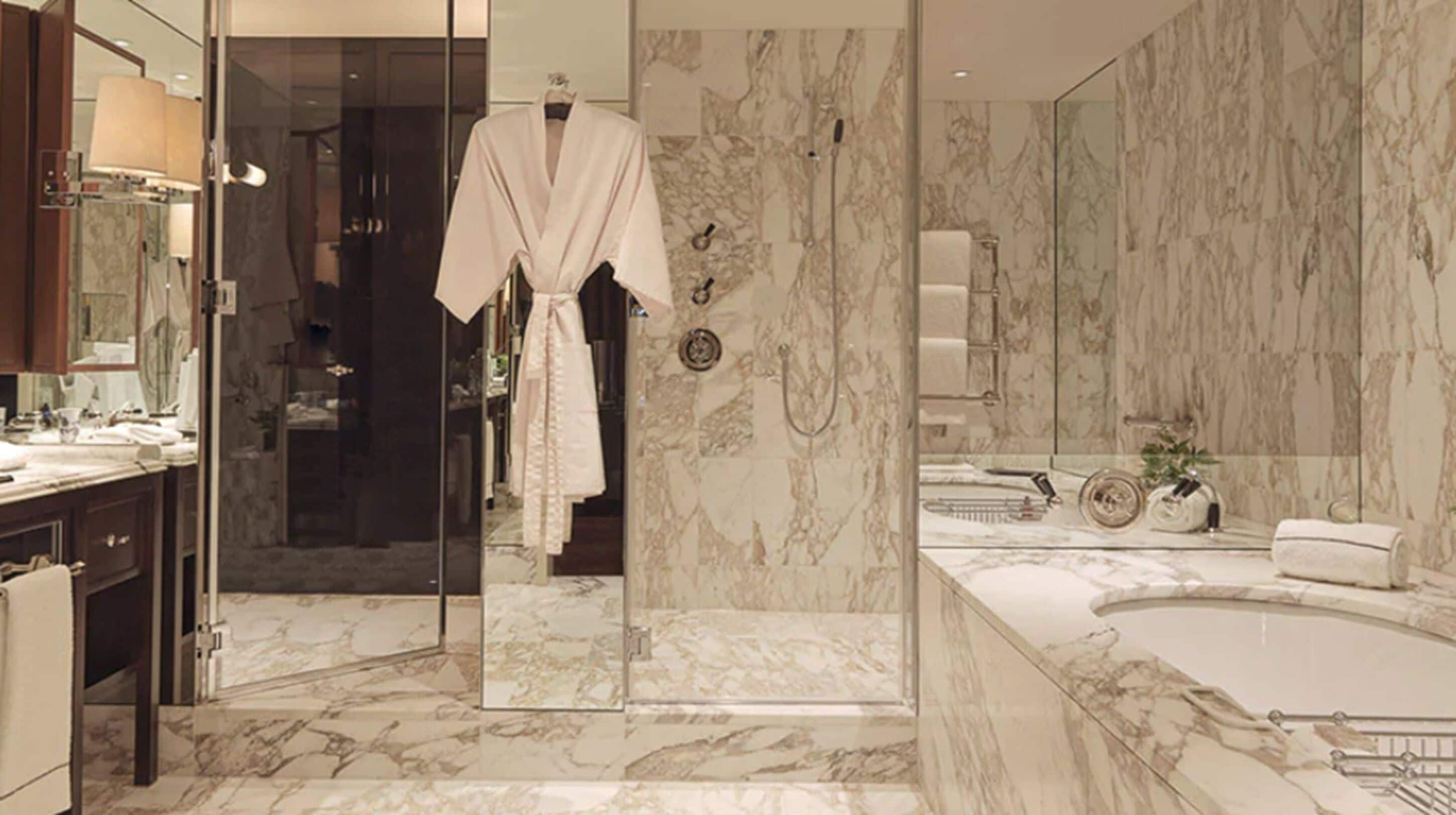 Un baño moderno con pisos de mármol, un espejo grande, una bañera y una bata colgada en una puerta.