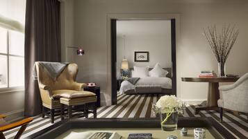 A hotel room with a large bed, a sitting area with a chair and a table, a view through an open door, and a vase with flowers on the table.