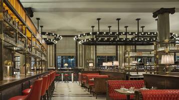 A bar area with red upholstered booths, a long counter with shelves of bottles, and a chandelier with multiple light fixtures.