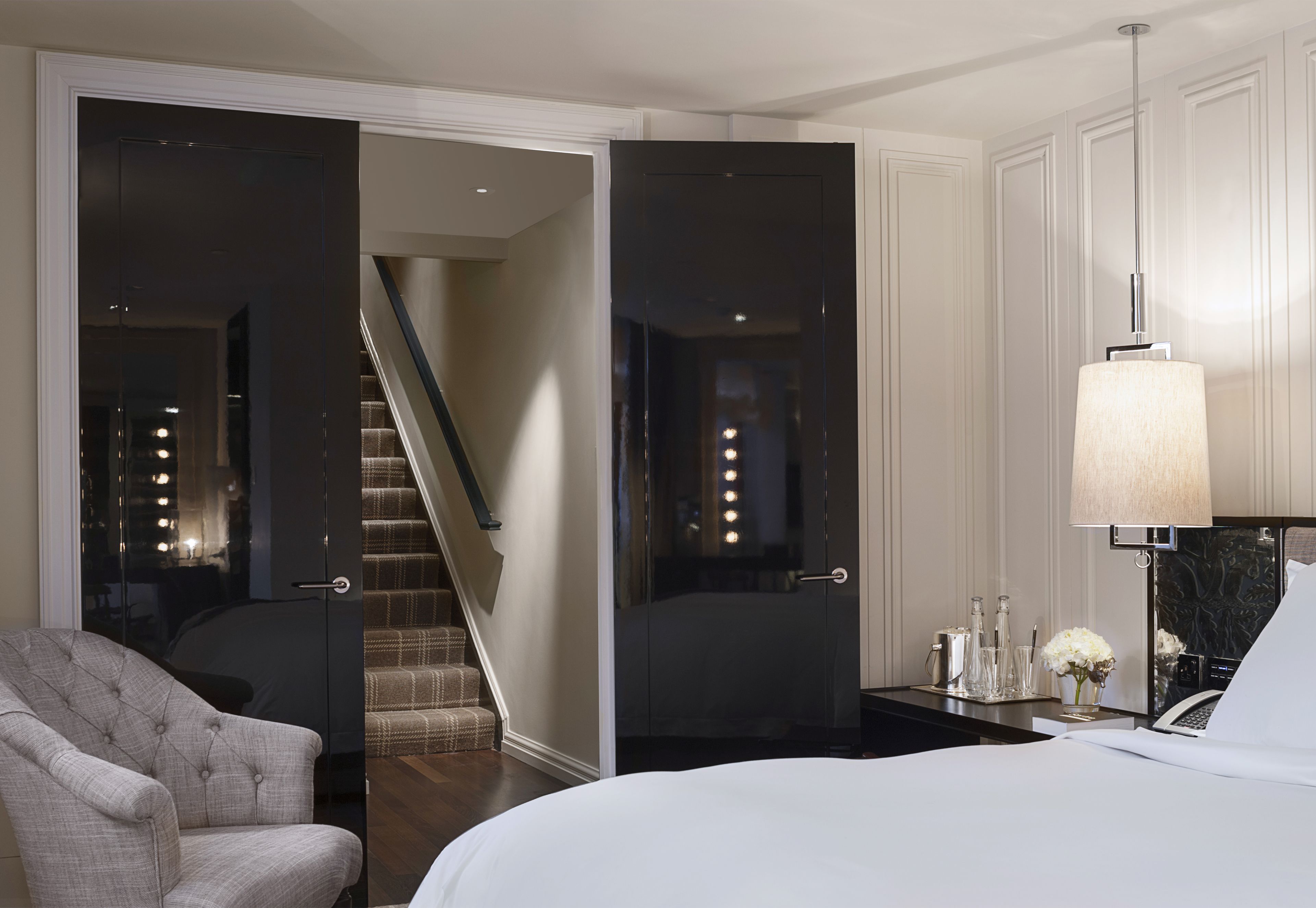 A hotel room with a bed, a chair, a desk with a lamp, and a staircase leading to another room.
