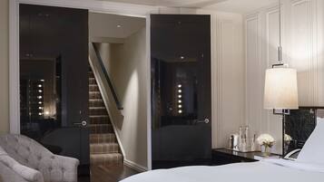 A hotel room with a bed, a chair, a desk with a lamp, and a staircase leading to another room.