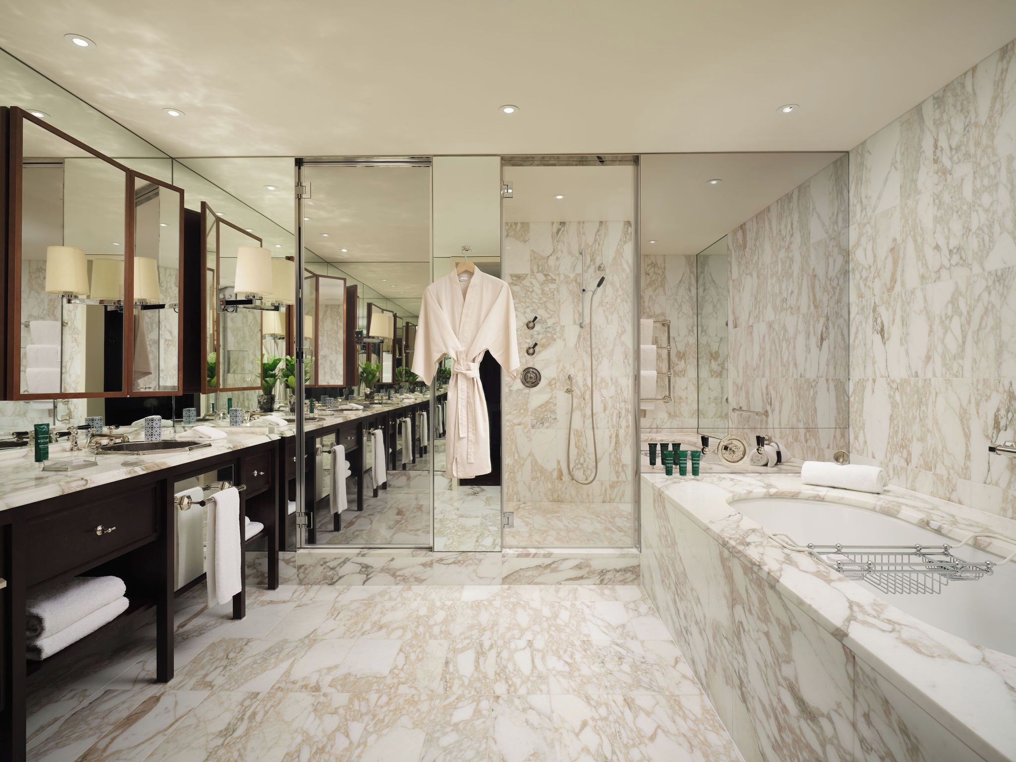 Ein luxuriöses Badezimmer mit Marmorboden, einer großzügigen Badewanne, einer großräumigen Dusche und einem langen Waschtisch mit mehreren Spiegeln und Waschbecken.