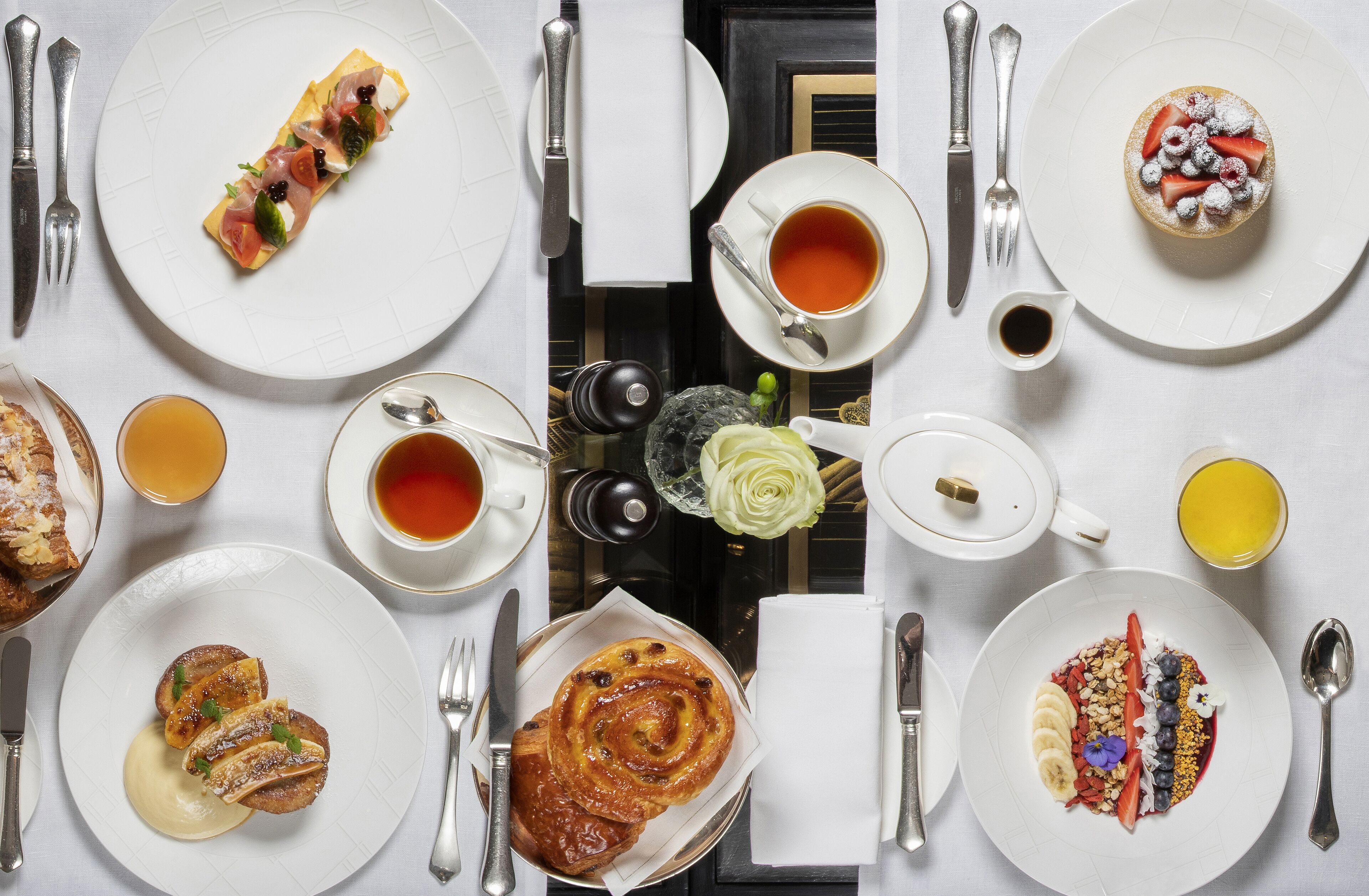 Une table mise pour le petit-déjeuner, avec différents plats, des tasses de thé et une théière.