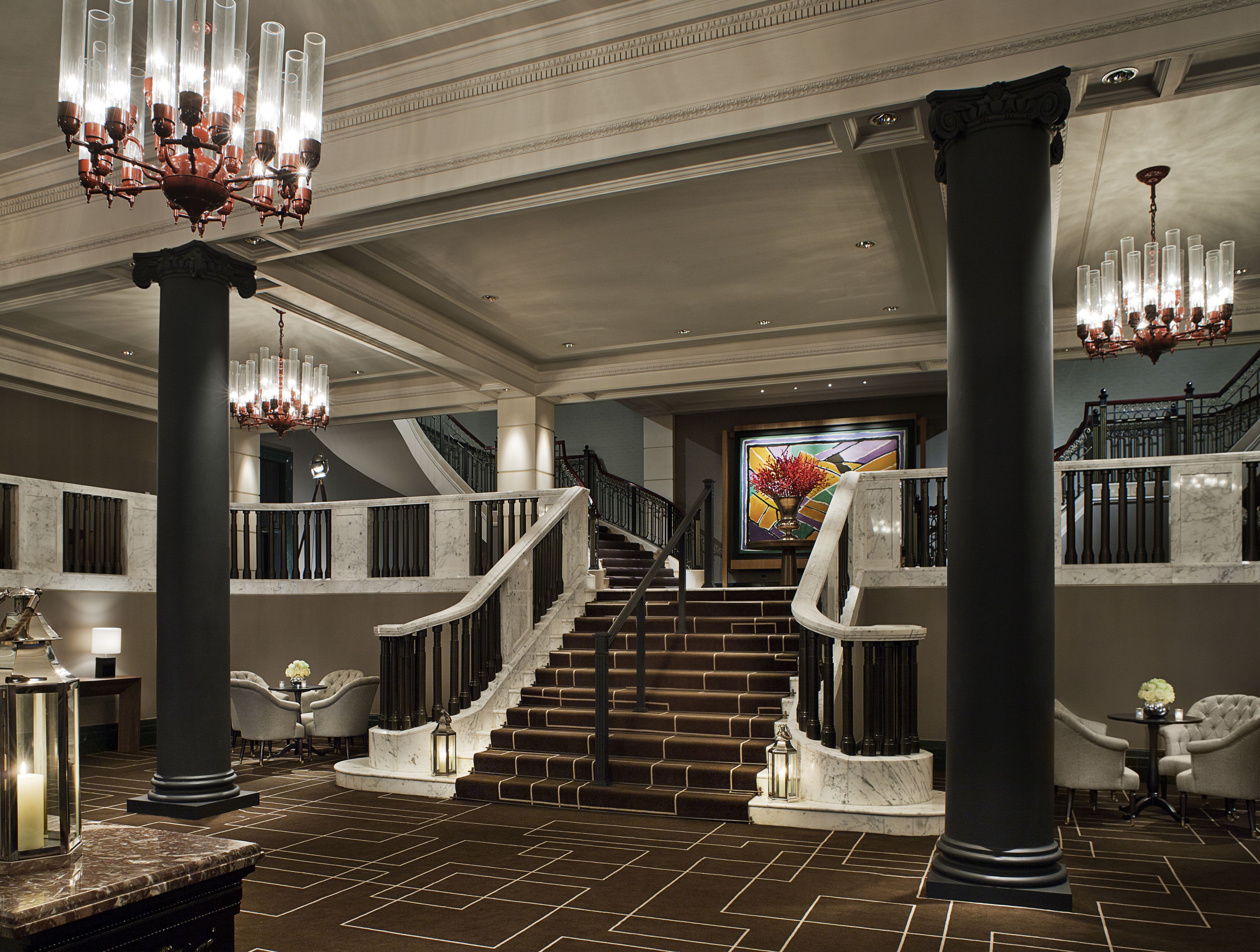 A grand lobby with a marble staircase, large columns, and chandeliers.