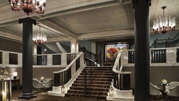 A grand lobby with a marble staircase, large columns, and chandeliers.