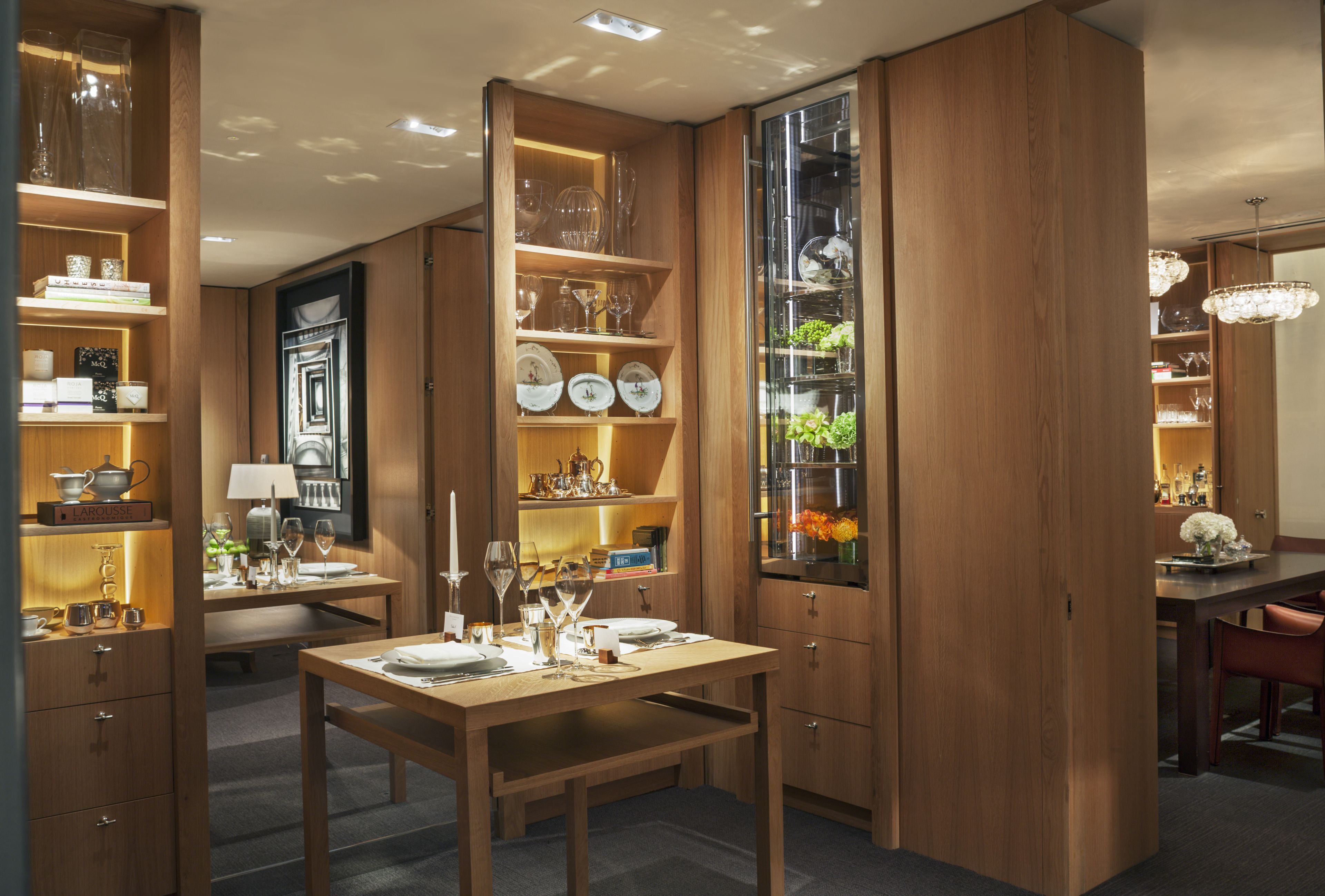 A well-lit dining area with wooden furniture, glassware, and decorative items on shelves.