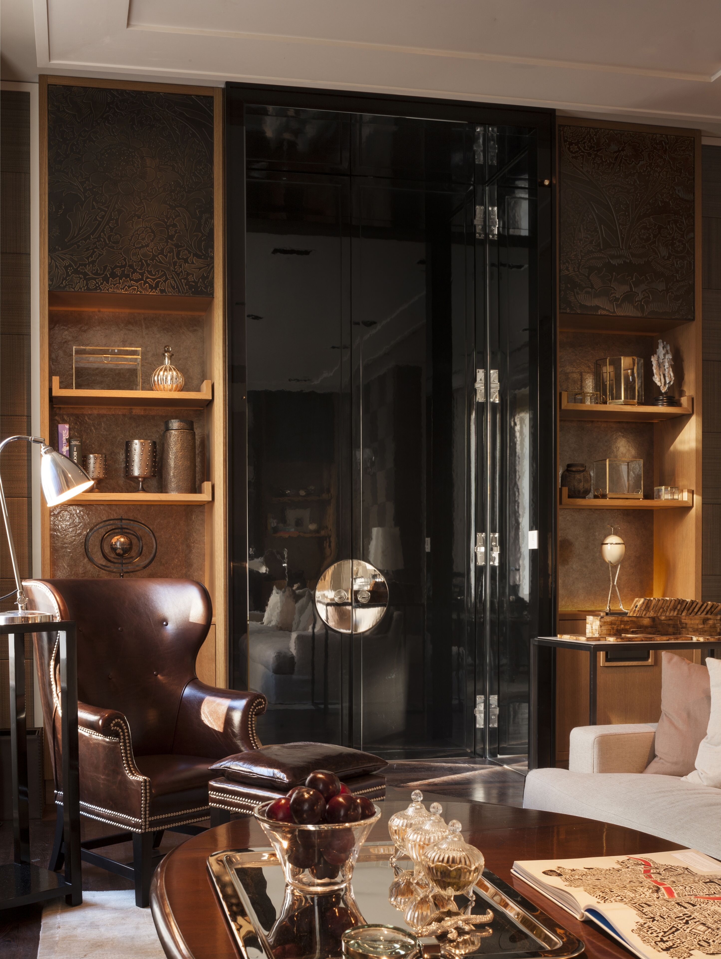 A modern living room with a leather armchair, a coffee table with decorative items, and a bookshelf with various objects.