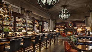 A bar area with a long counter, multiple bar stools, and a fireplace. There are bookshelves and a large globe decoration on the wall. - Rosewood London (London)